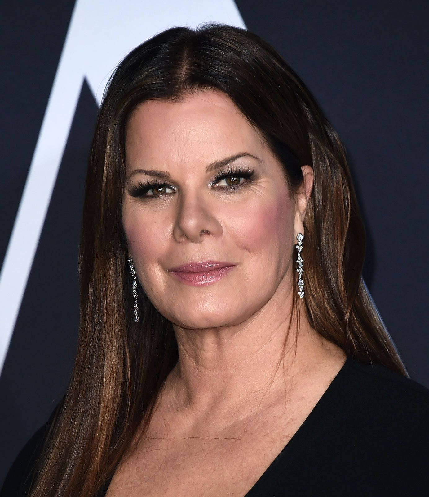 Celebrity 桌布 壁紙 — 一位長髮棕髮女性的特寫肖像，戴著閃亮的鑽石耳環和黑色上衣，背景為深色帶有白色幾何形狀。