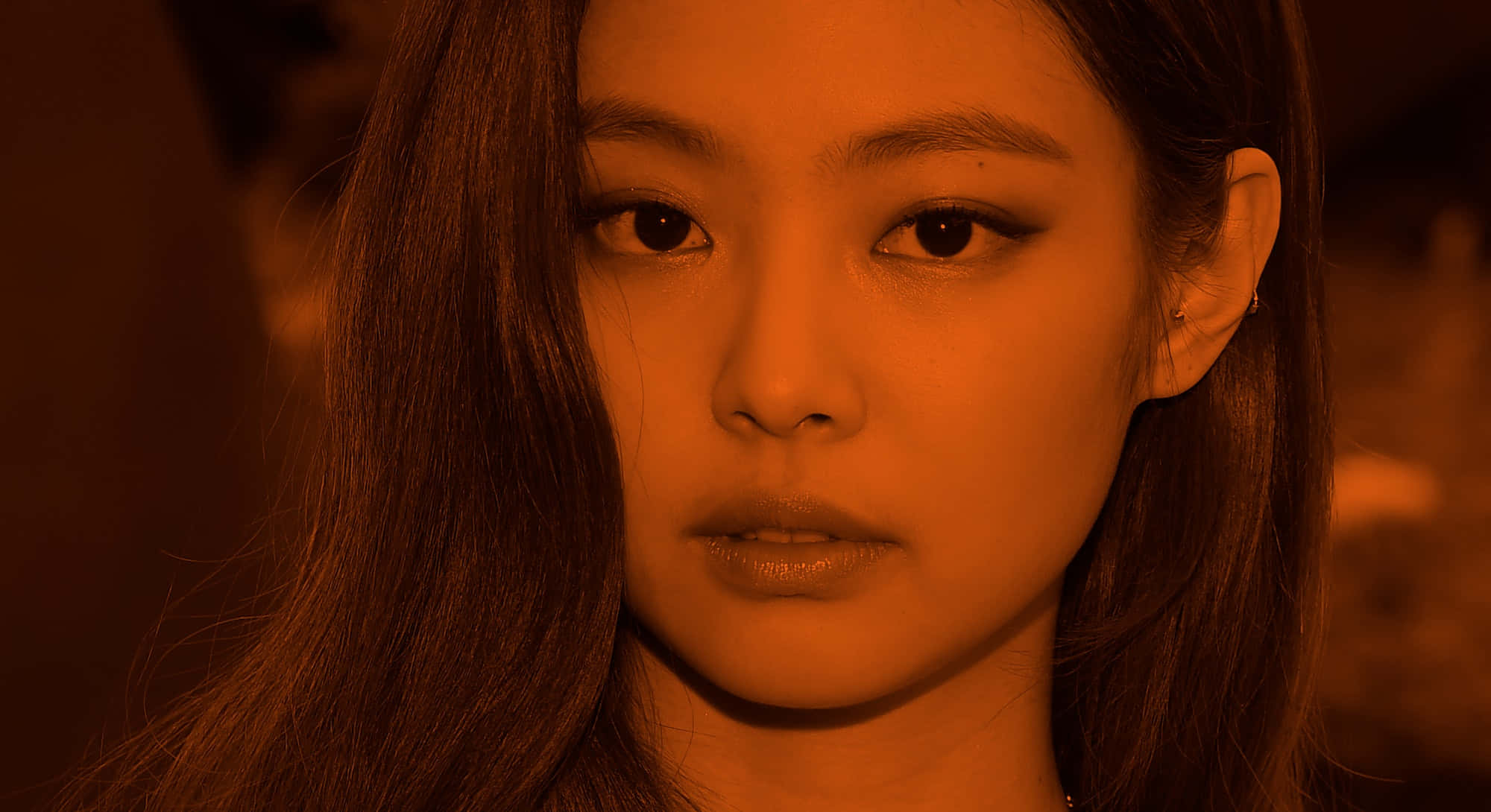 BLACKPINK 桌布 壁紙 — 一位長髮深色女子的特寫肖像，在溫暖的橙色燈光下，她專注的目光直視前方。