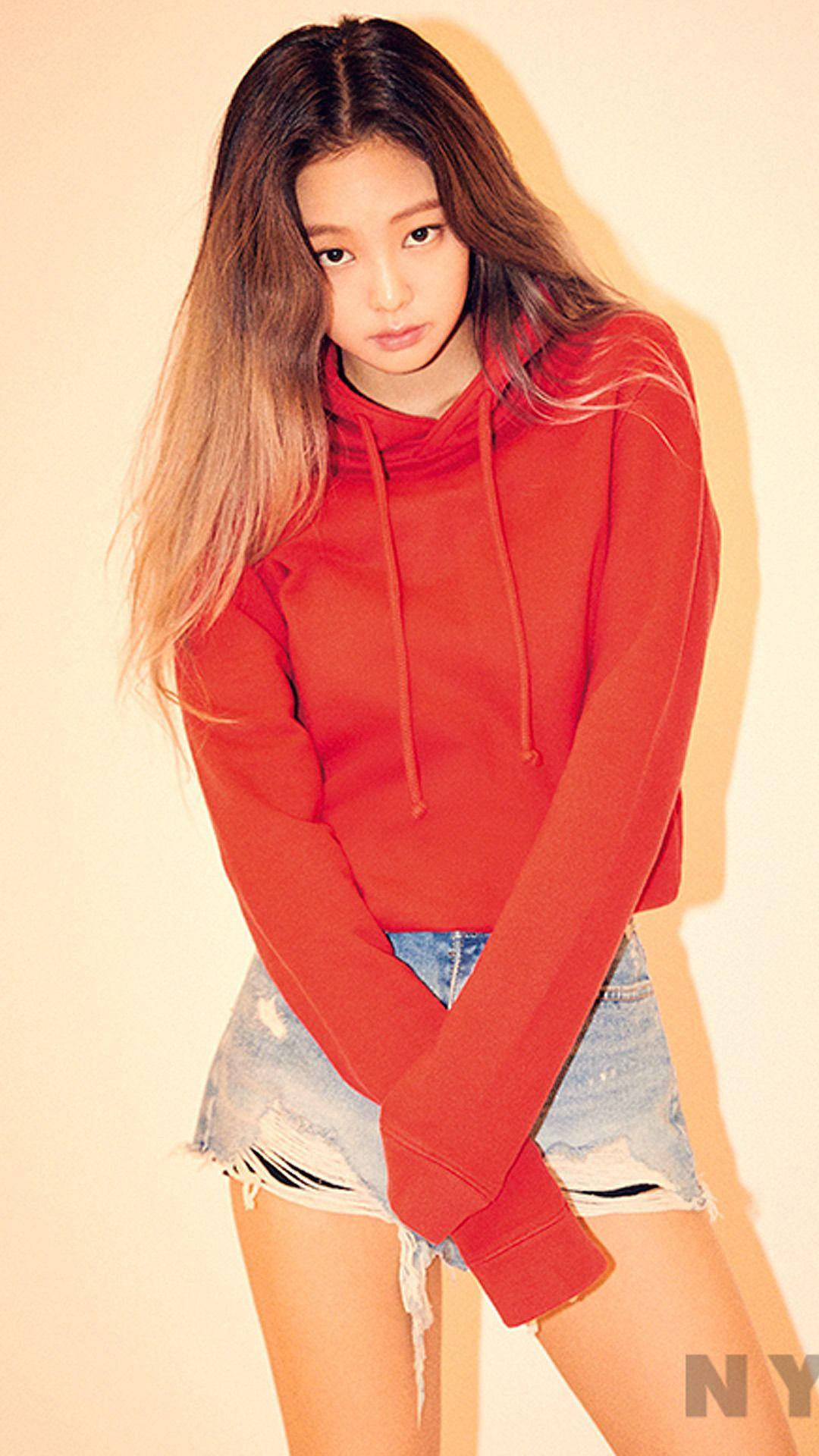 Jennie 桌布 壁紙 — 一位長髮漸層染的年輕女性，穿著紅色連帽衫和破洞牛仔短褲，背景是純米色牆壁。
