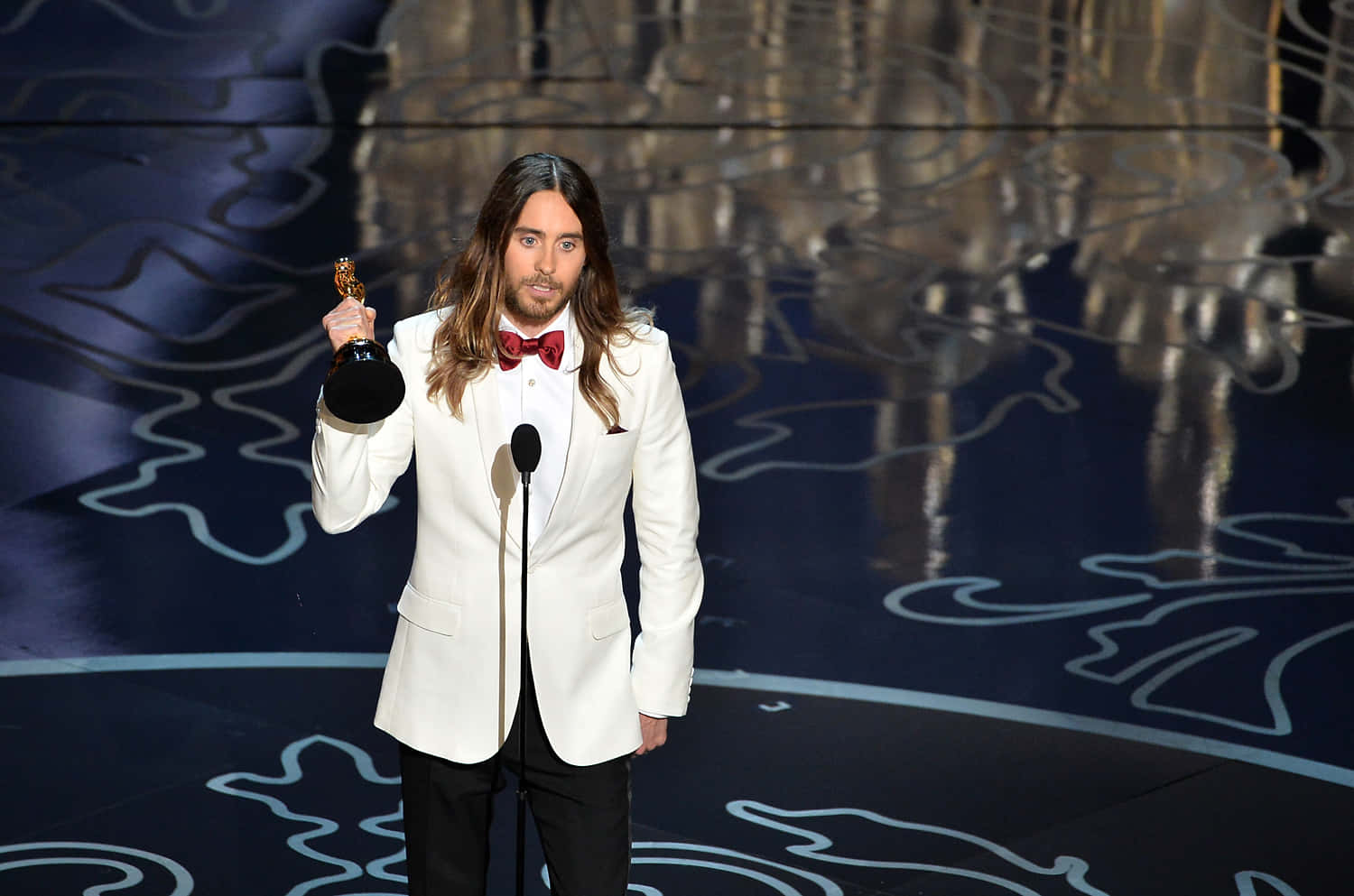 jared leto 桌布 壁紙 — 一位長髮男子身穿白色燕尾服，在圖案舞台的明亮燈光下手持奧斯卡獎座。
