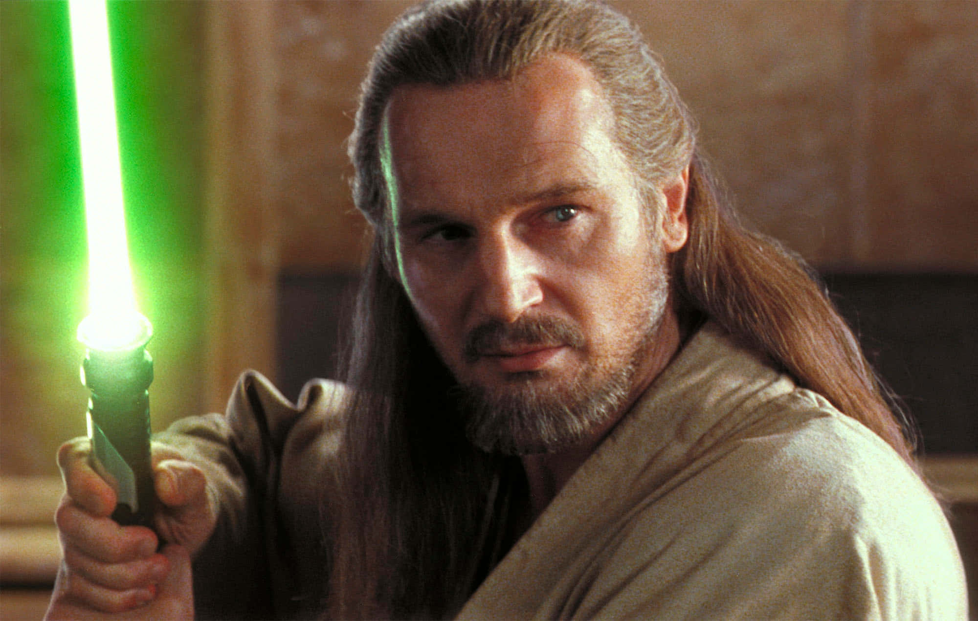 The Phantom Menace 桌布 壁紙 — 一位長髮的絕地大師在光線昏暗、帶有溫暖石牆的房間中手持發光的綠色光劍。