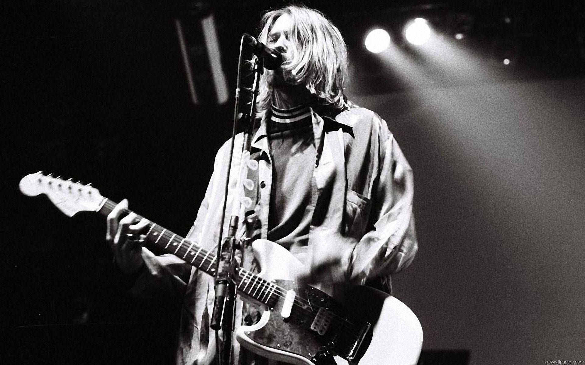 Cobain 桌布 壁紙 — 一位長髮音樂家在黑白照片中，於明亮的舞台燈光下熱情地彈奏白色電吉他。