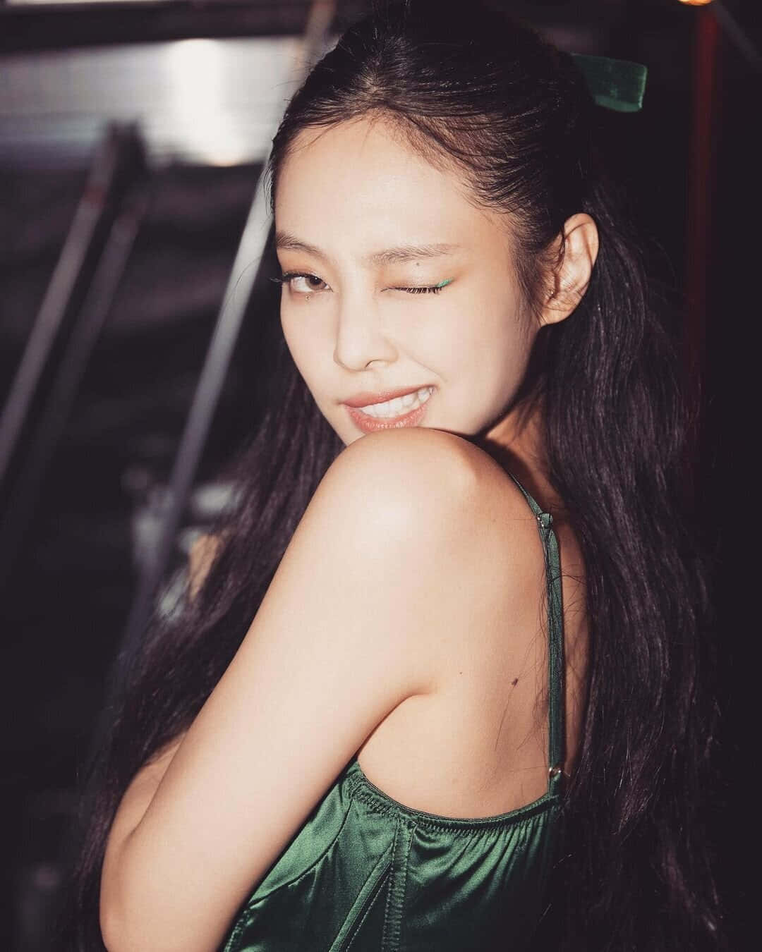BLACKPINK 桌布 壁紙 — 一位長黑髮、綠色眼影的女性，在昏暗的室內環境中穿著閃亮的綠色連衣裙，頑皮地微笑。