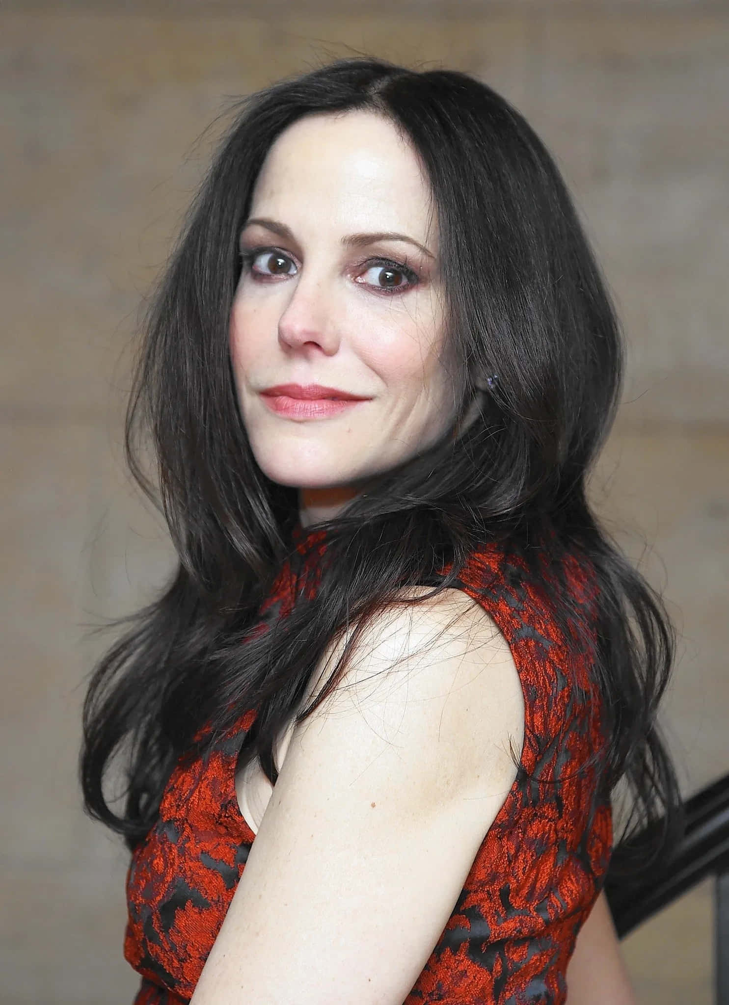 mary louise parker 桌布 壁紙 — 一位長黑髮、身穿紅色圖案上衣的女性，帶著含蓄的微笑回頭望向肩膀後方。