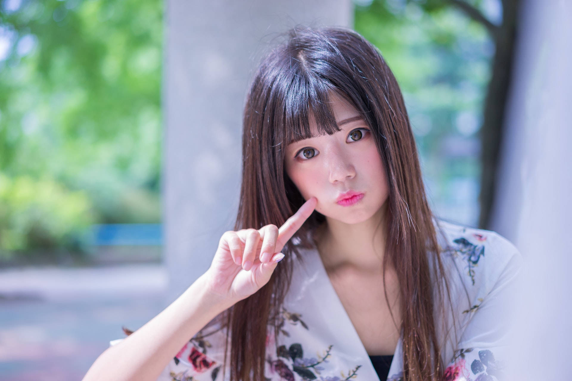 lovely girl 桌布 壁紙 — 一位長黑髮、身穿花卉和服的年輕女性，在陽光普照的戶外環境中，輕輕觸碰臉頰，同時直視鏡頭。