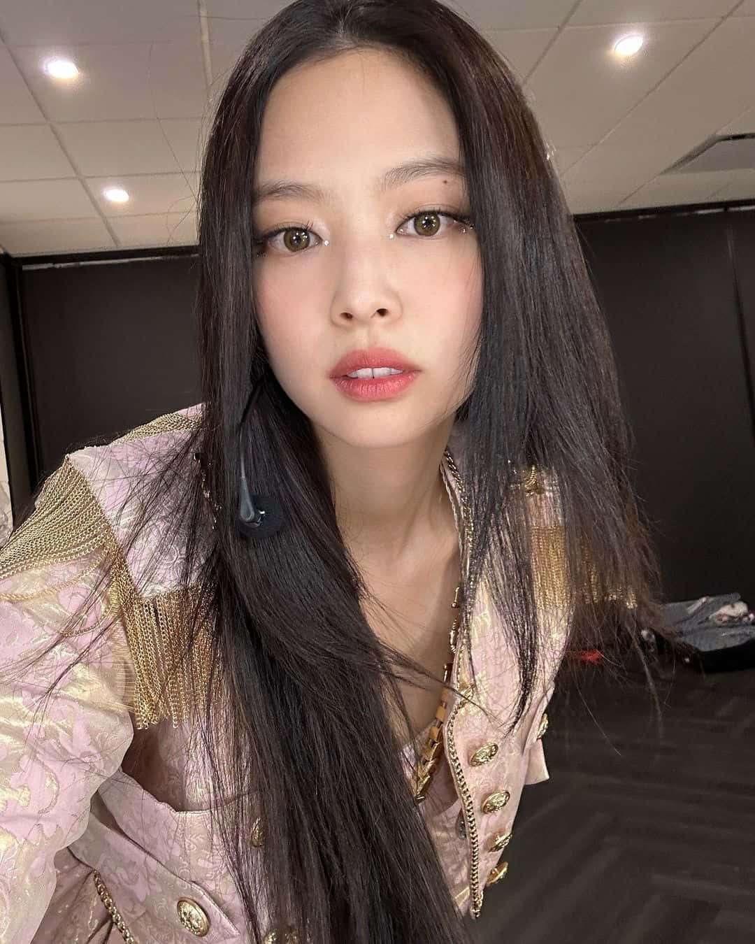 K-pop 桌布 壁紙 — 一位長黑髮女性在室內穿著粉紅和金色裝飾外套的 close-up 自拍。