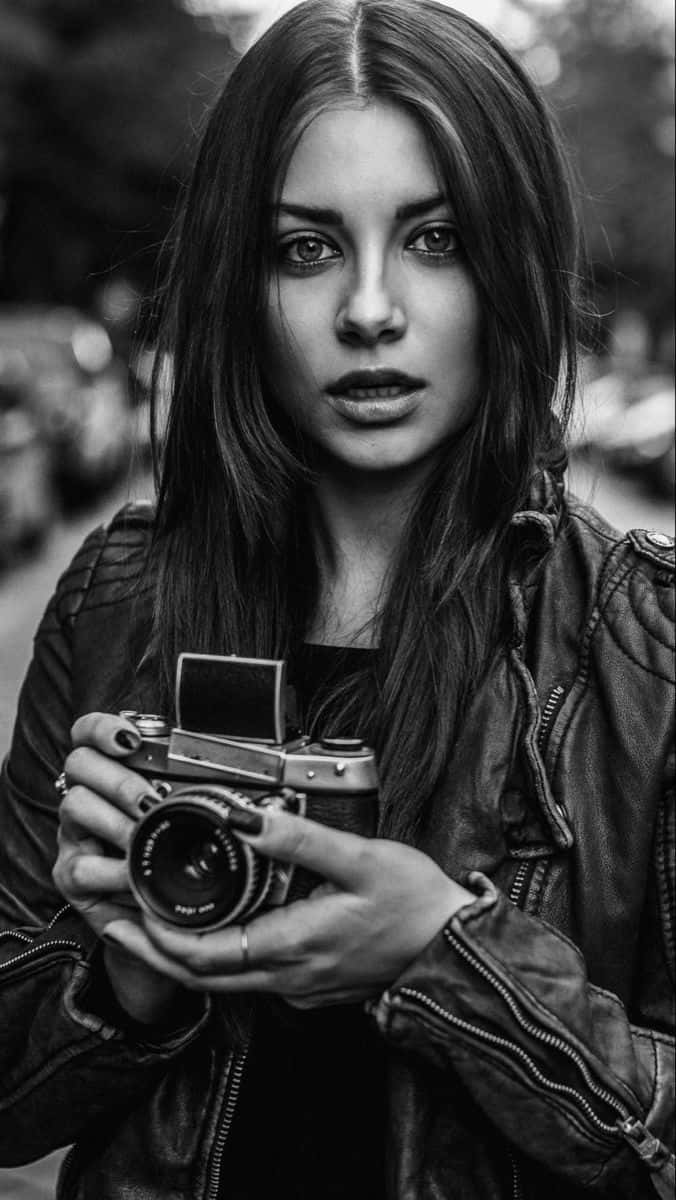 Holding Camera 桌布 壁紙 — 一位長黑髮女性穿著皮夾克手持復古底片相機的黑白肖像。