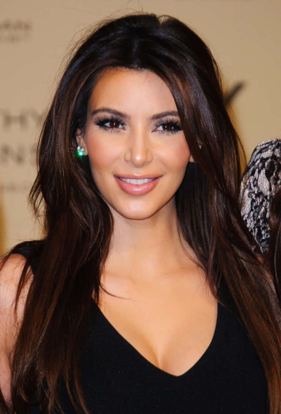 Kim Kardashian 桌布 壁紙 — 一位長黑髮女性穿著黑色上衣和綠色耳環對著鏡頭微笑的特寫肖像。