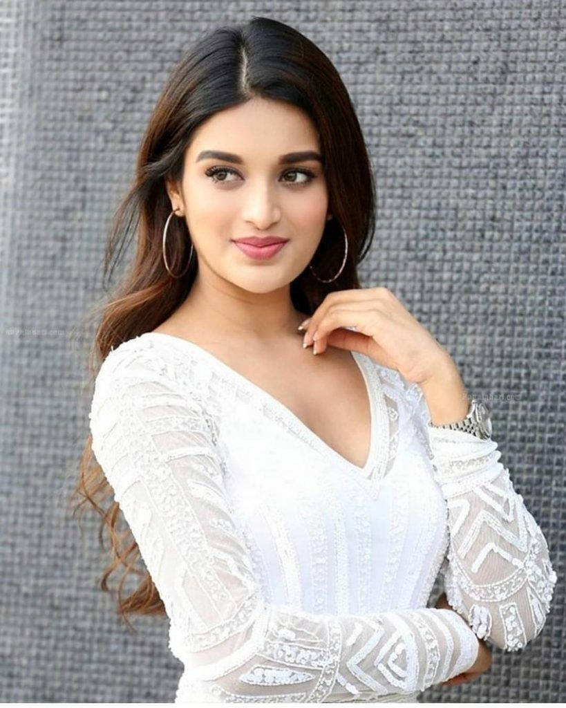 Telugu Heroines 桌布 壁紙 — 一位長黑髮戴著圈圈耳環的女性，穿著華麗的白色蕾絲上衣，在灰色紋理牆前溫柔微笑。
