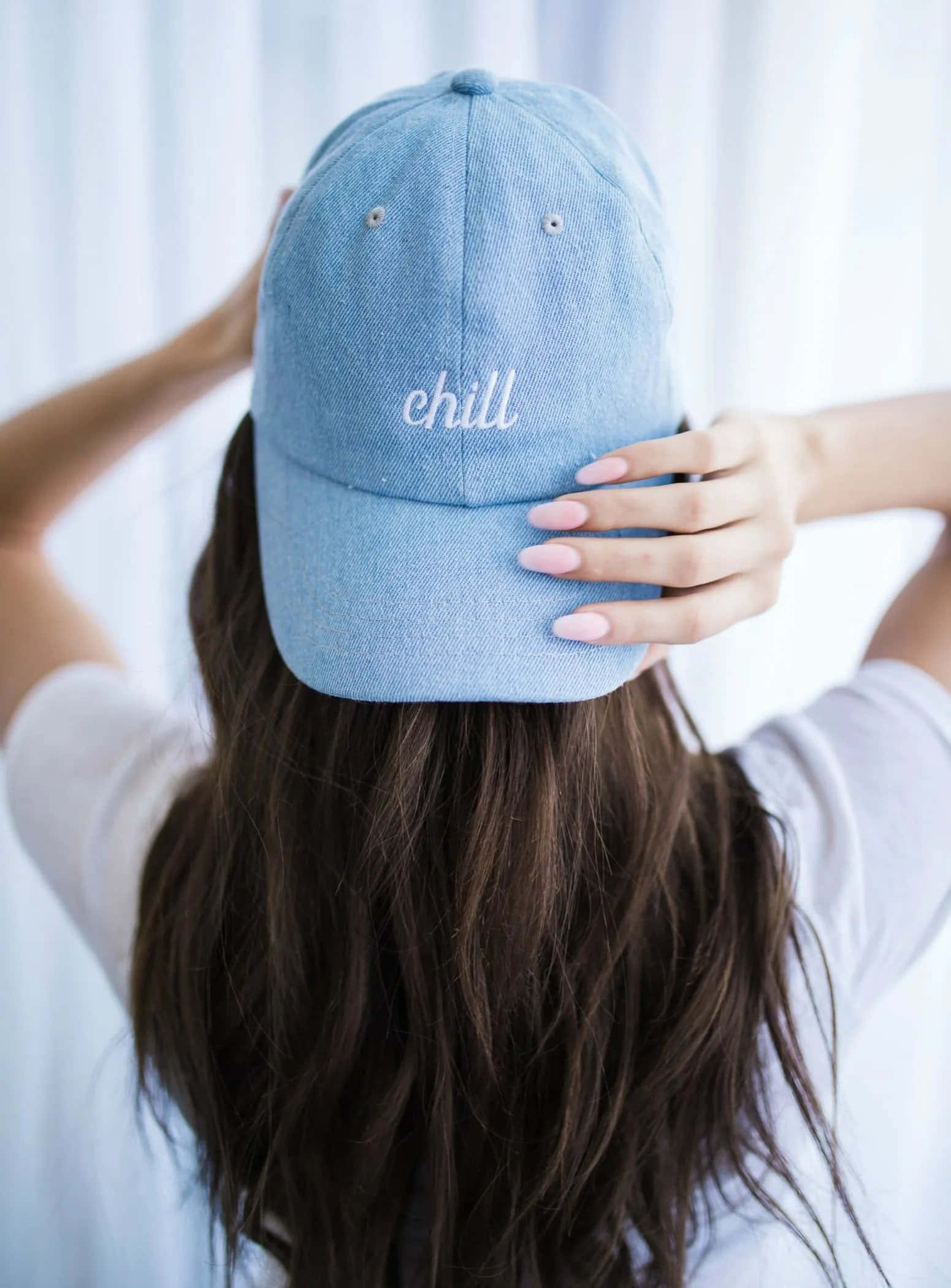 Woman 桌布 壁紙 — 一位長黑髮的人戴著淺藍色牛仔帽，帽上繡有白色「chill」字樣，室內站在薄紗窗簾旁。