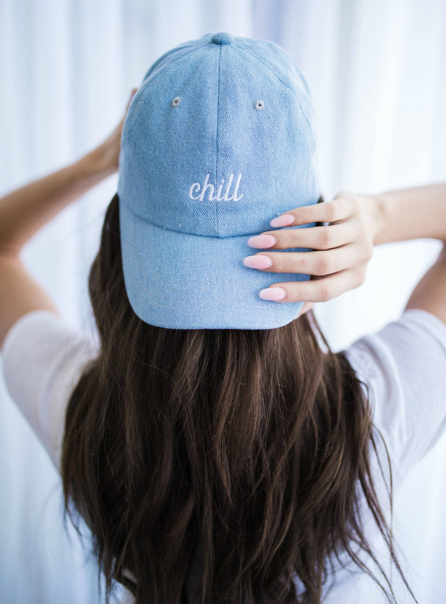 Cap 桌布 壁紙 — 一位長黑髮的人戴著淺藍色牛仔帽，帽上繡有白色的「chill」字樣，正在調整帽子。