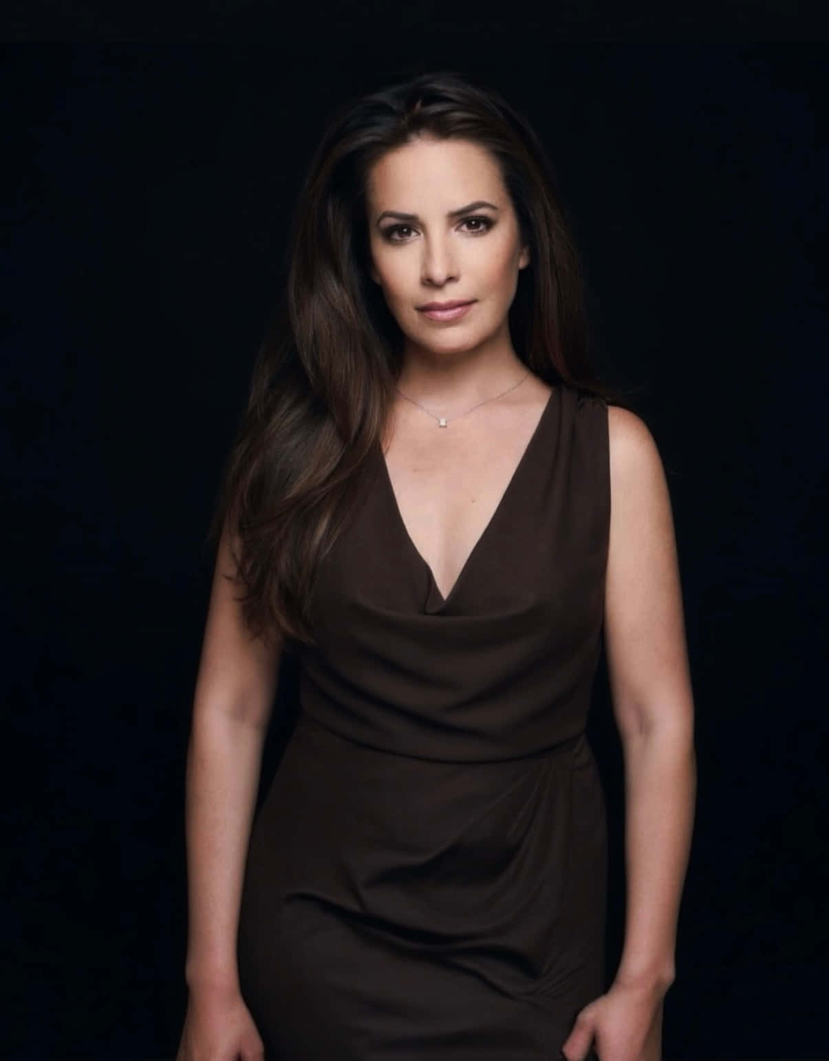 Charmed Season 7 Promotional Image - Holly Marie Combs 壁紙 — 一位長黑髮的優雅女性在工作室肖像中穿著棕色連衣裙，背景是純黑色。
