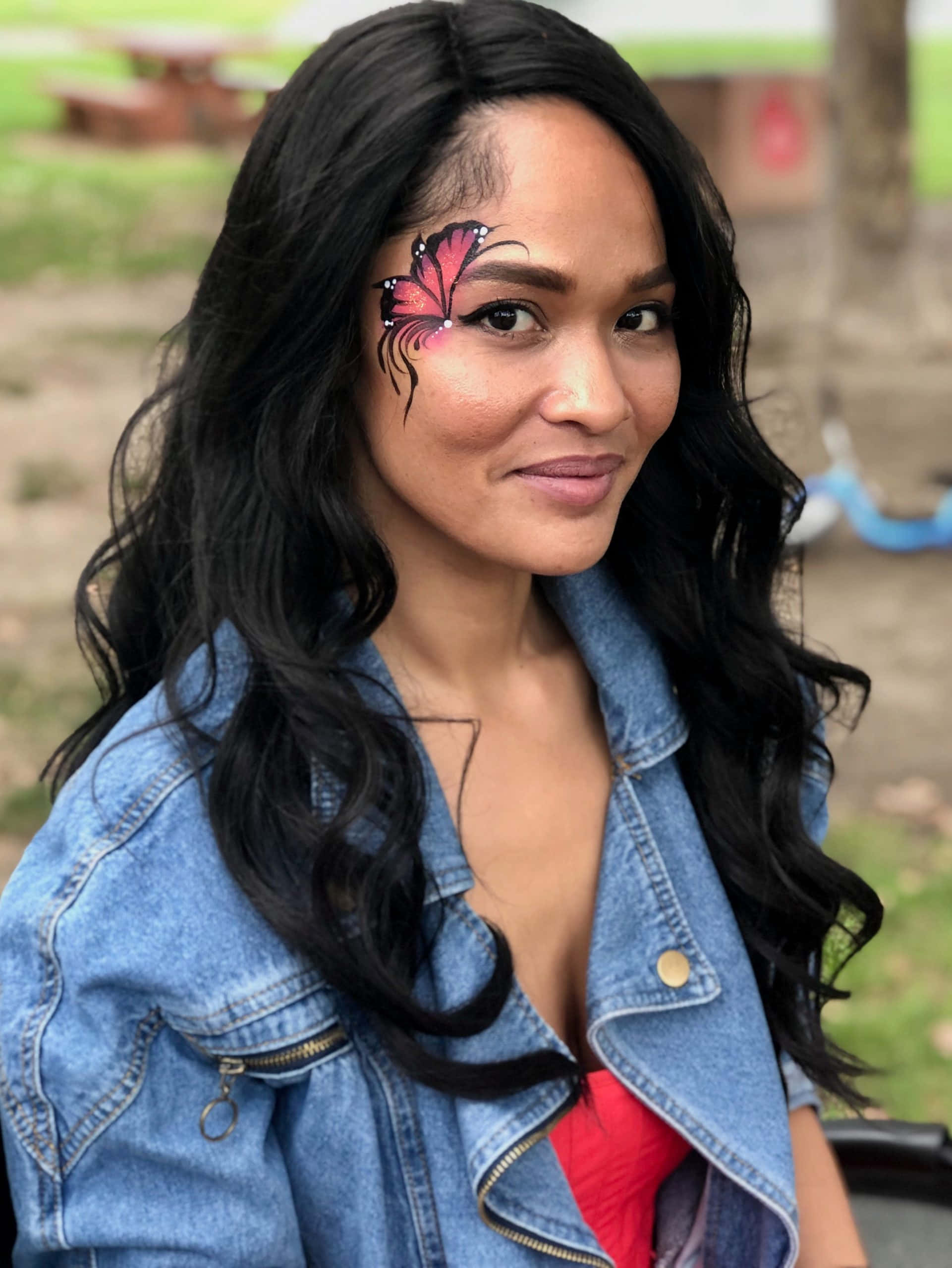 Butterfly Face Painting 桌布 壁紙 — 一位長黑髮的女性，眼睛附近有蝴蝶臉部彩繪，穿著牛仔外套在戶外微笑。