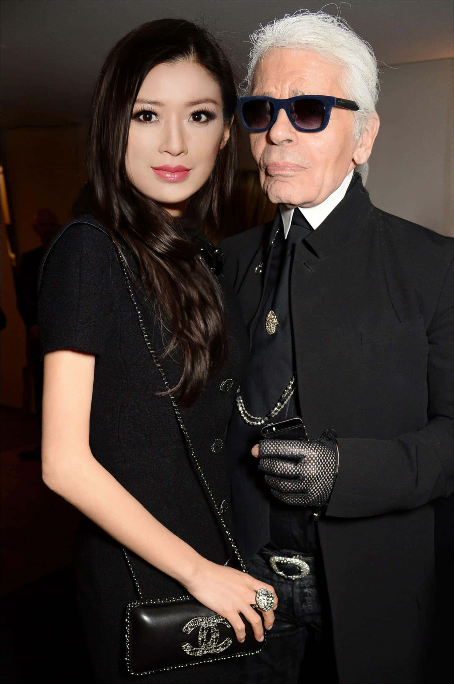 Karl Lagerfeld 桌布 壁紙 — 一位長黑髮的女性和一位白髮戴太陽眼鏡的男性在室內活動中穿著黑色正裝一起擺姿勢。