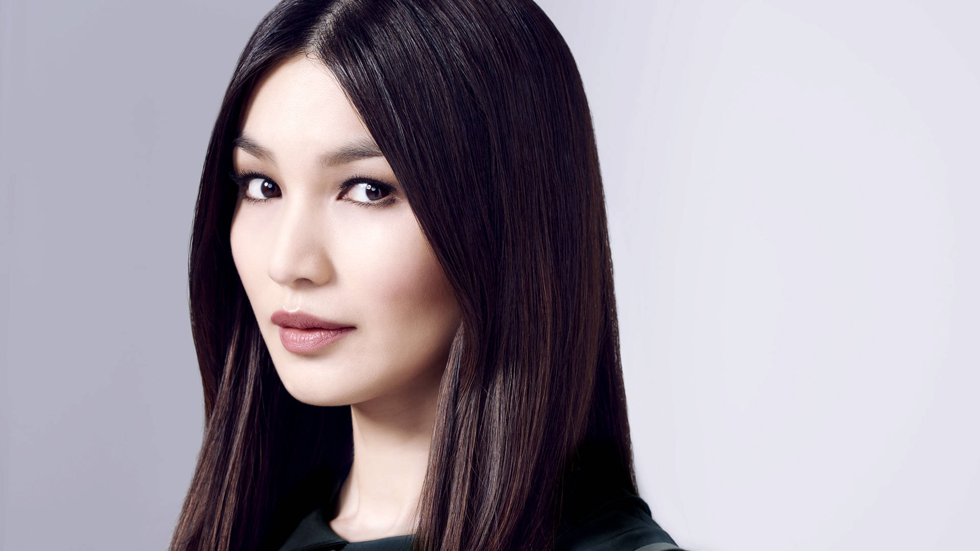 Gemma Chan 桌布 壁紙 — 一位長黑髮的女性在工作室肖像中，對著純灰色背景柔和地凝視。