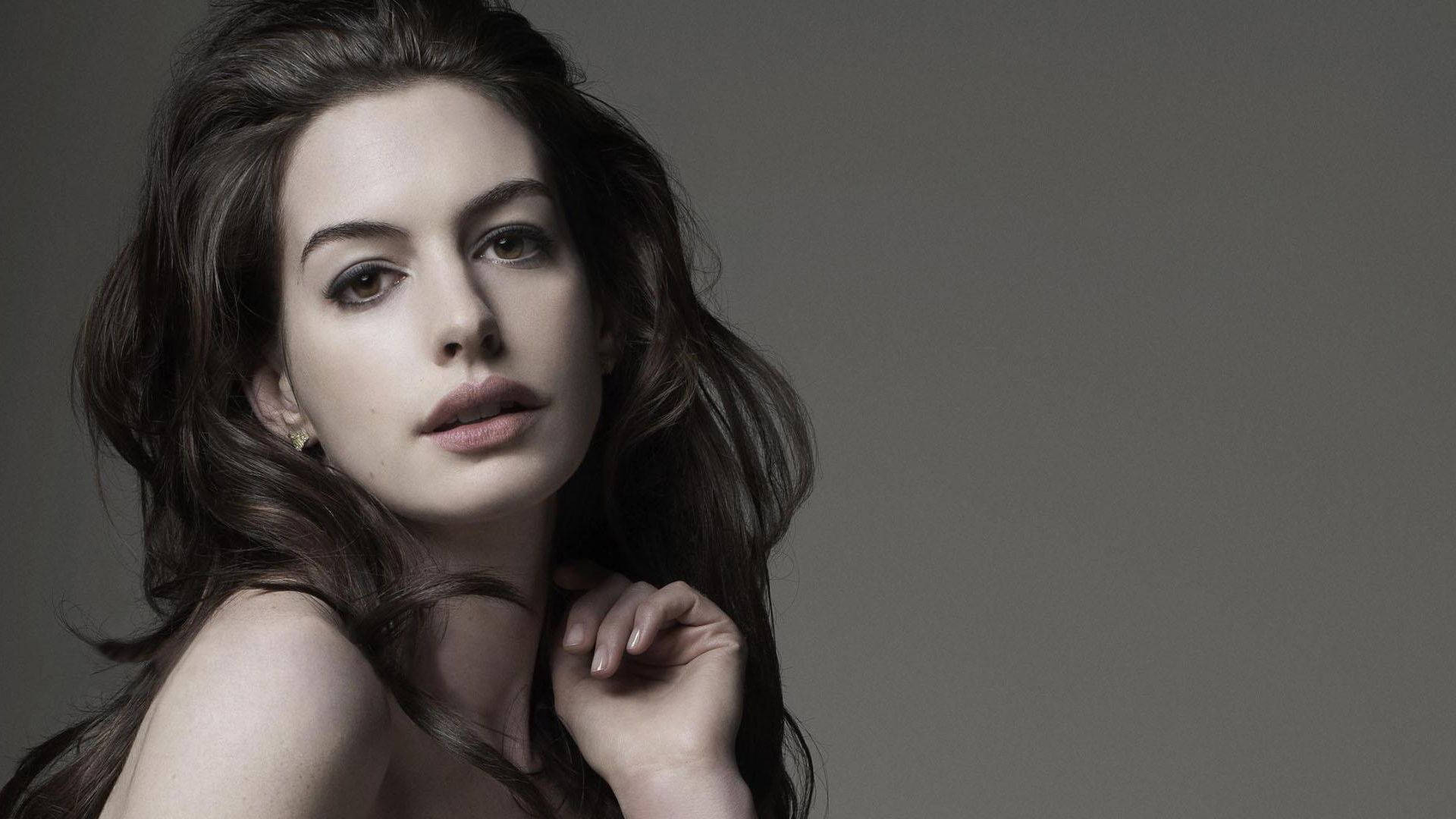Anne Hathaway 桌布 壁紙 — 一位長黑髮的女性在柔和的灰色背景下溫柔地凝視著相機。