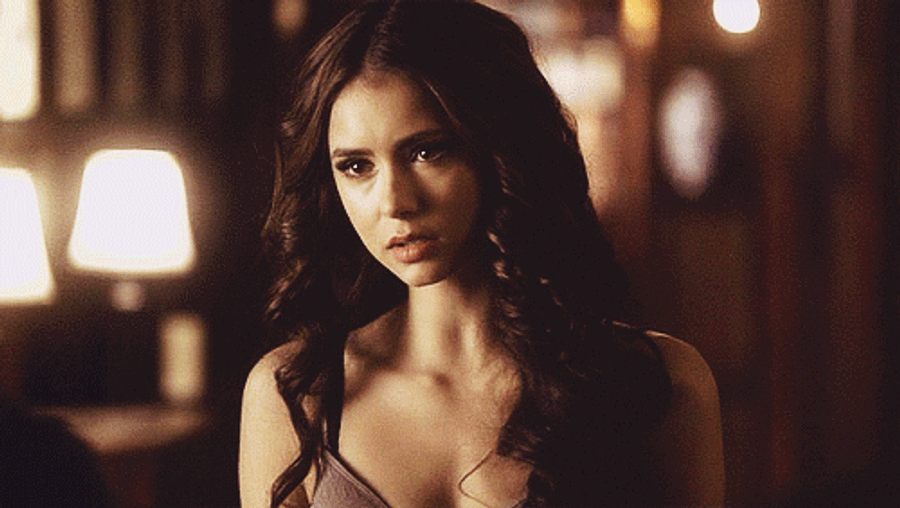 Vampire Diaries 桌布 壁紙 — 一位長黑髮的女性在溫暖昏暗的房間中，背景有柔和發光的燈，專注地凝視著。