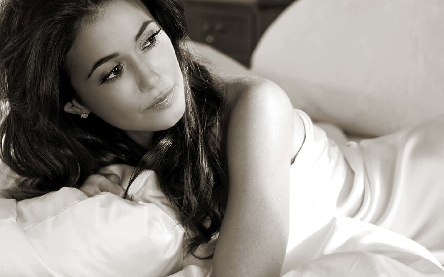 Emmanuelle Chriqui 桌布 壁紙 — 一位長黑髮的女性在黑白肖像中將頭靠在枕頭上，若有所思地向上凝視。