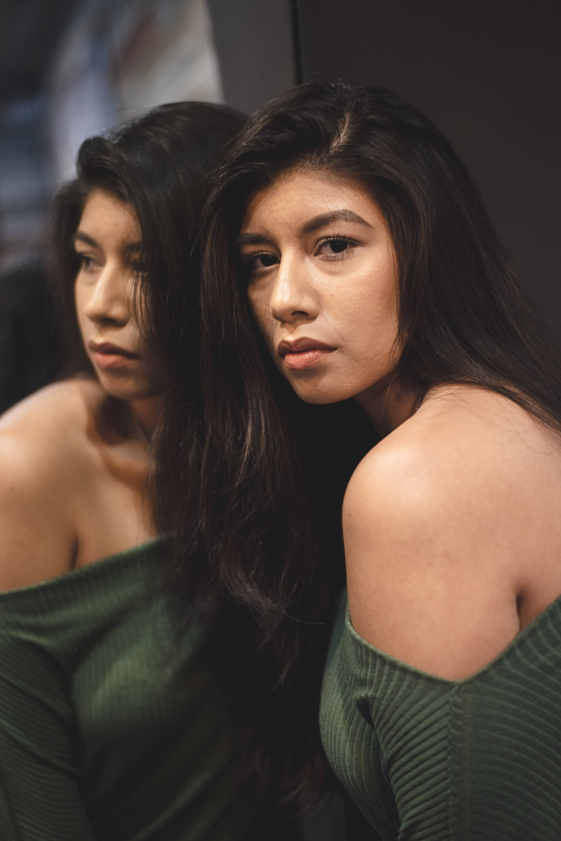 Mexican Woman 桌布 壁紙 — 一位長黑髮的女性專注地凝視，而她的倒影在昏暗的房間中顯示出憂鬱的表情。