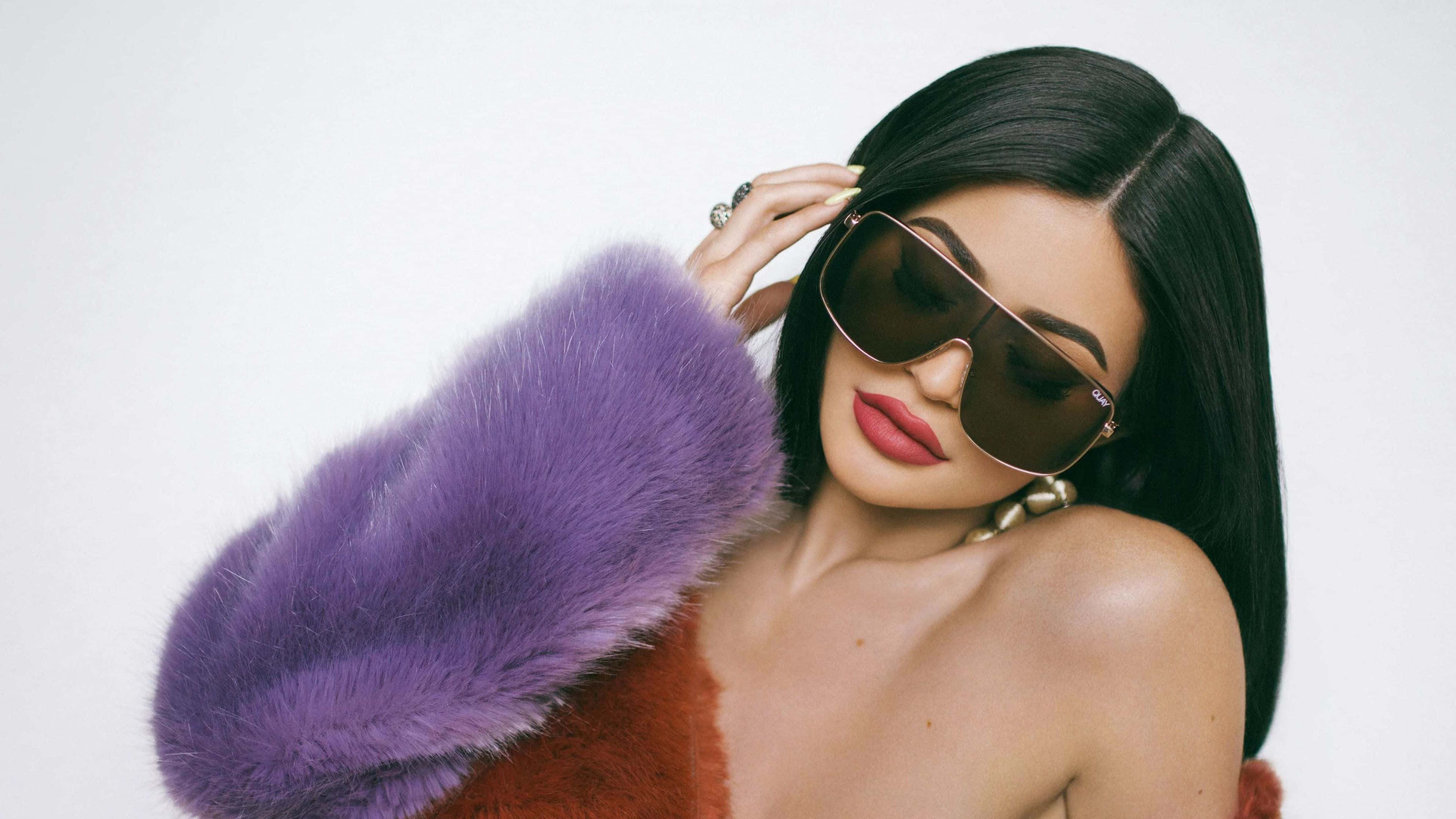 Kylie Jenner 4K 桌布 壁紙 — 一位長黑髮的女性戴著超大太陽眼鏡和紫色毛袖，背景為純白色。