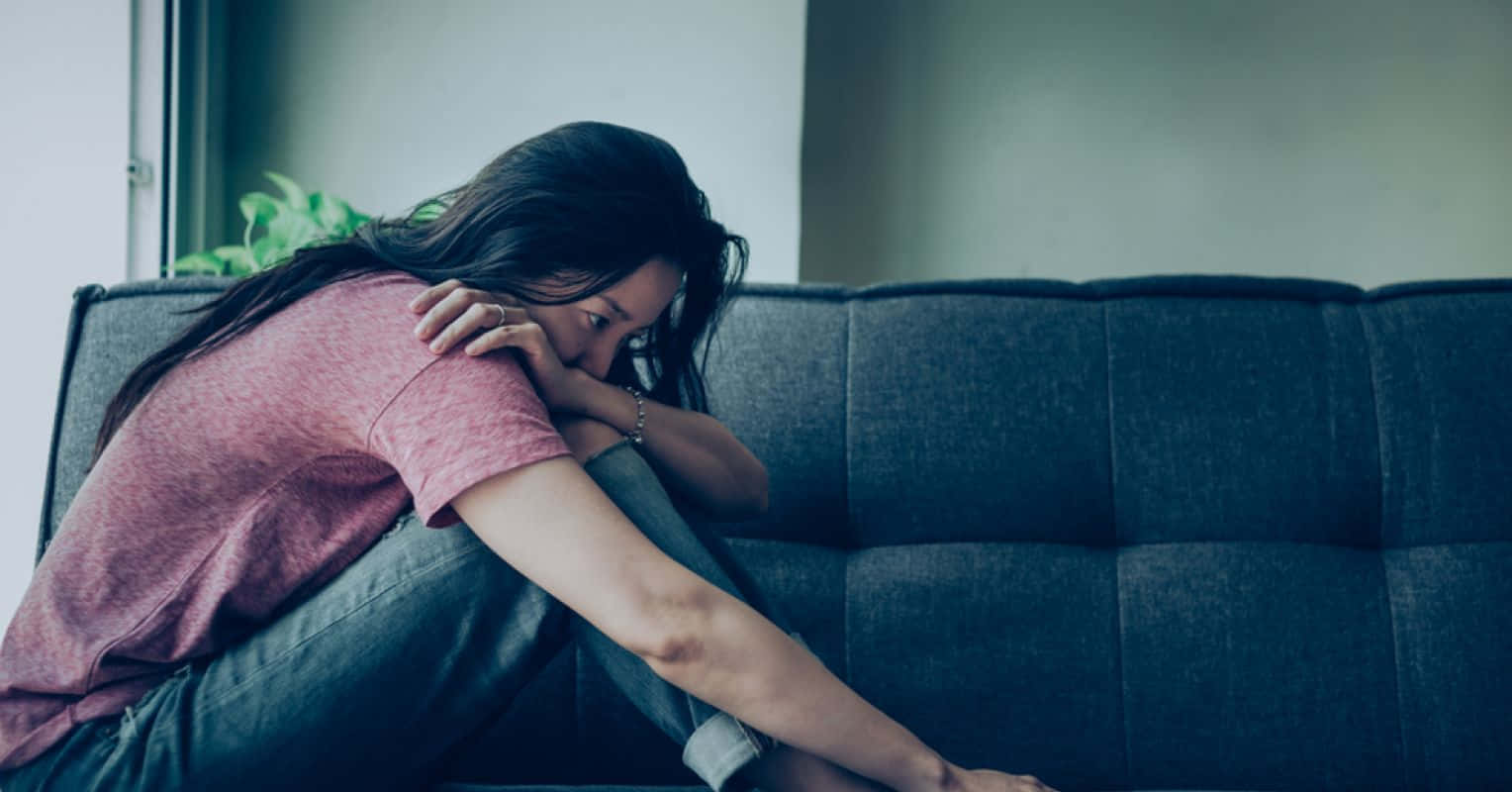 Lonely 桌布 壁紙 — 一位長黑髮的女性癱坐在深藍色沙發上，頭靠在手臂上，沉浸在寂靜的悲傷中。