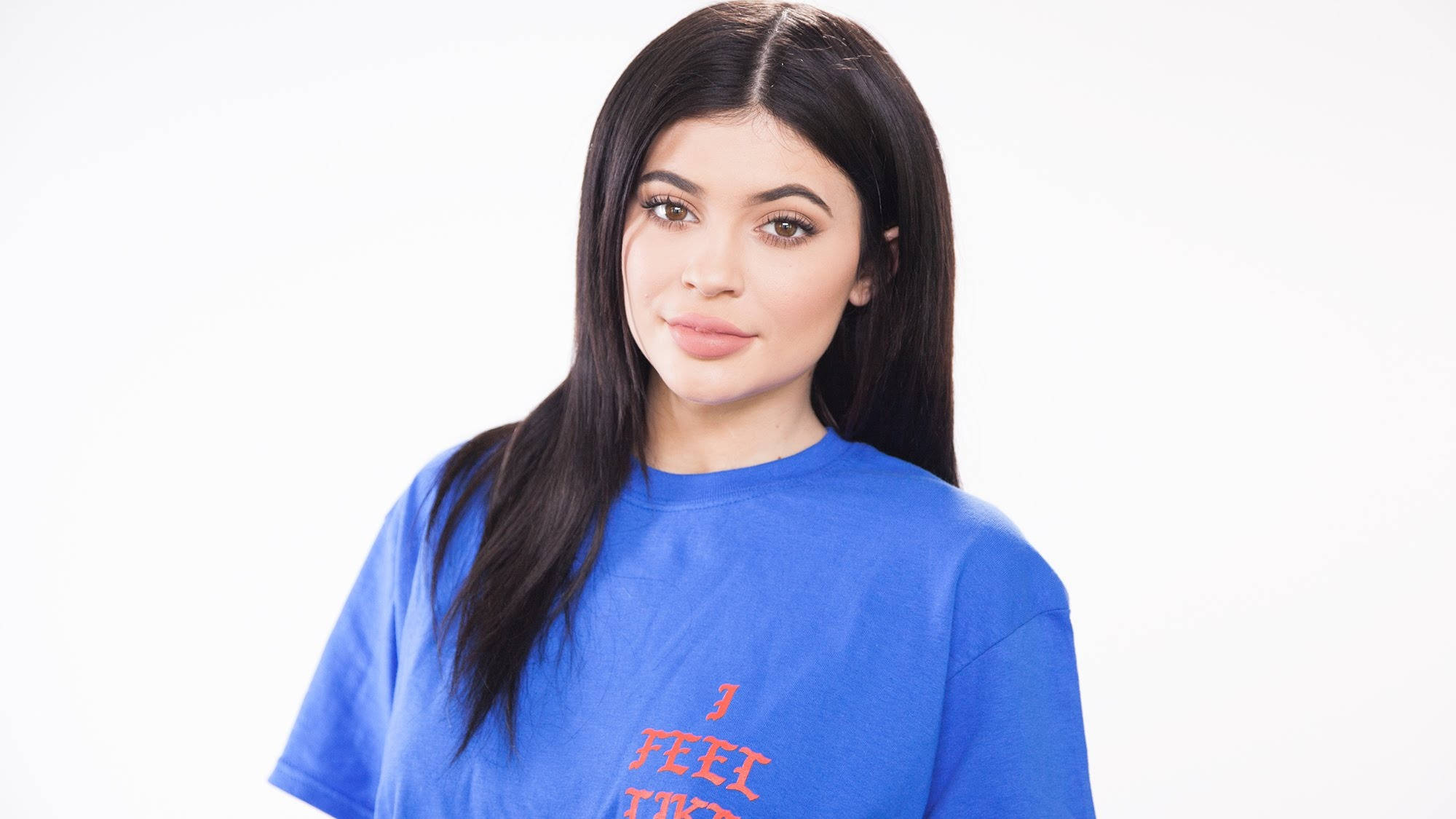 Kylie 桌布 壁紙 — 一位長黑髮的女性穿著藍色T恤，上面有紅色文字，背景是純白色。