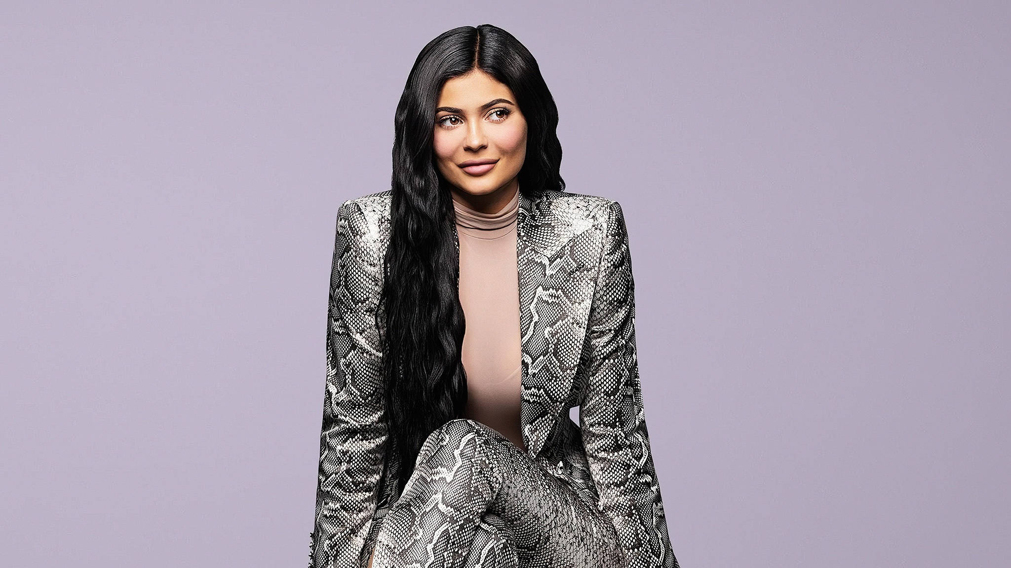 Kylie 桌布 壁紙 — 一位長黑髮的女性穿著銀色蛇紋套裝，背景是柔和的薰衣草色。