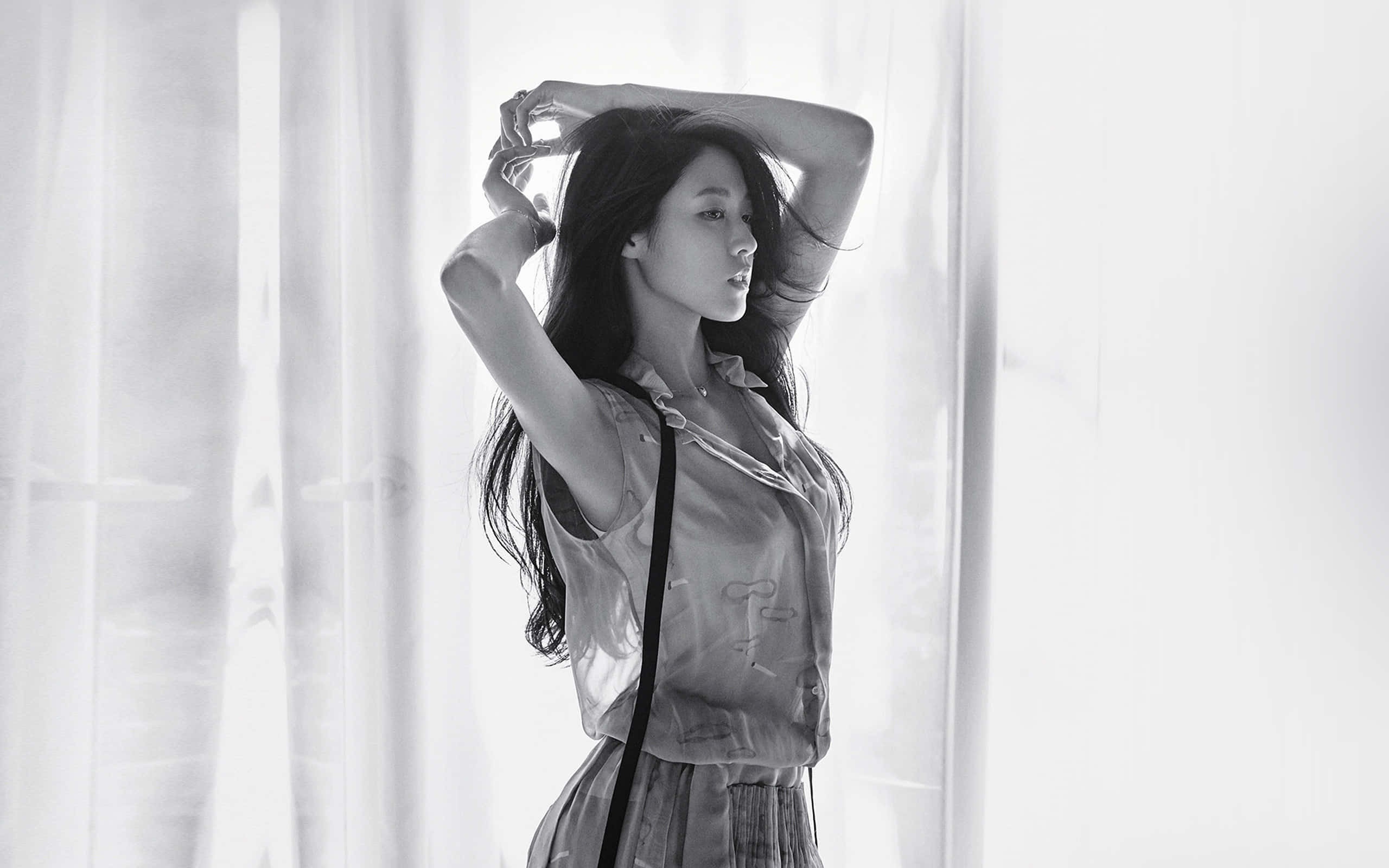 Photoshoot 桌布 壁紙 — 一位長黑髮的女性站在薄紗窗簾旁，雙臂舉起，陽光從她身後過濾進來，形成一幅單色肖像。