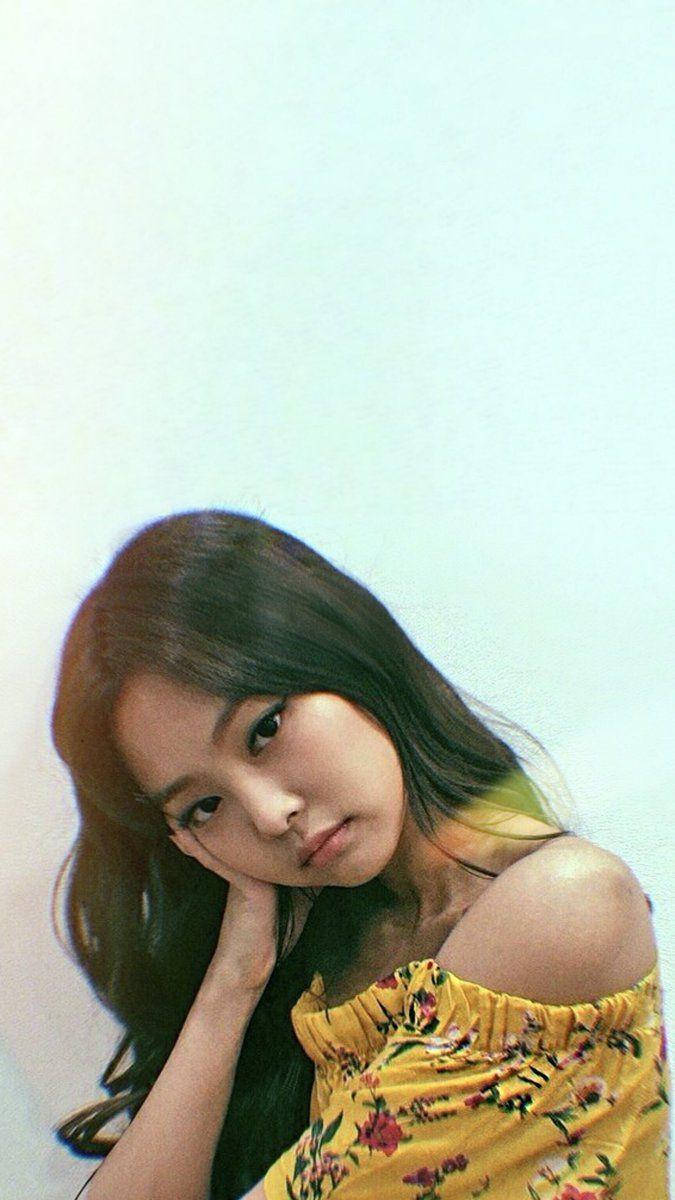 Jennie 桌布 壁紙 — 一位長黑髮的年輕女子，身穿黃色花卉露肩上衣，在柔和的淺藍色背景前，將頭靠在手上。