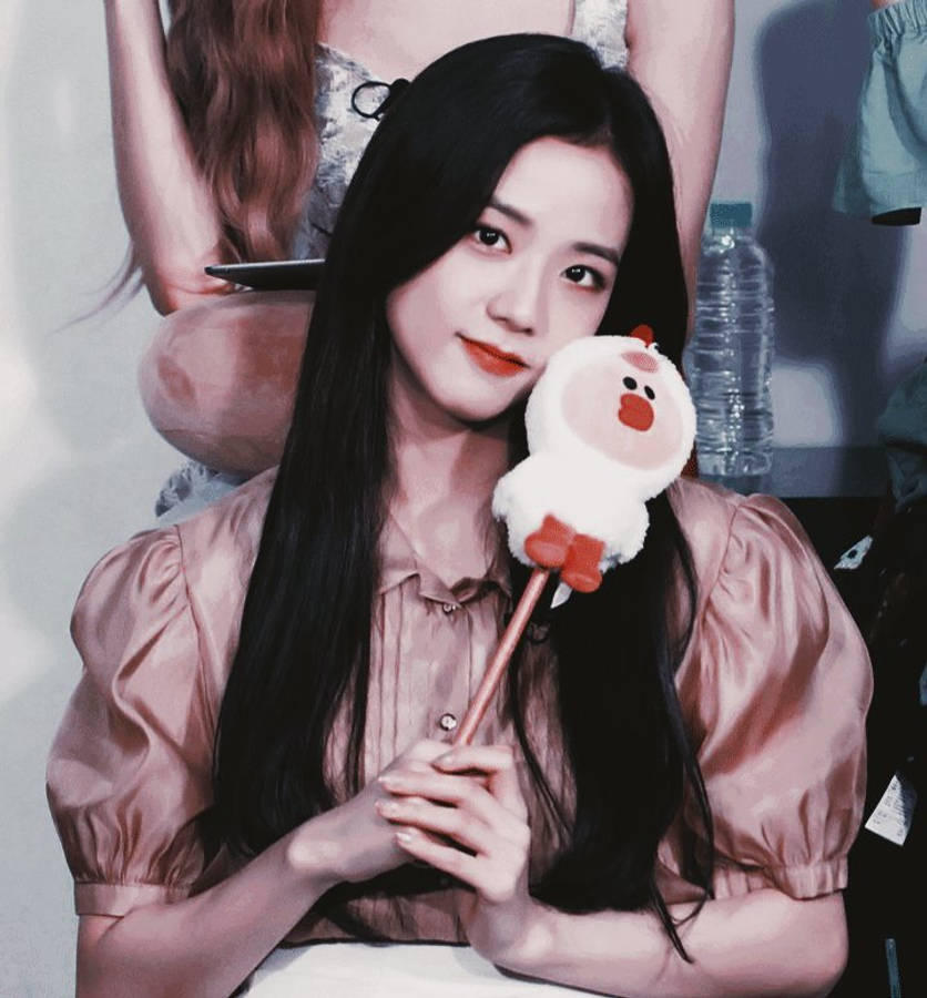 Jisoo Cute 桌布 壁紙 — 一位長黑髮的年輕女子微笑著，輕輕拿著一根棍子上的毛絨雞玩偶。