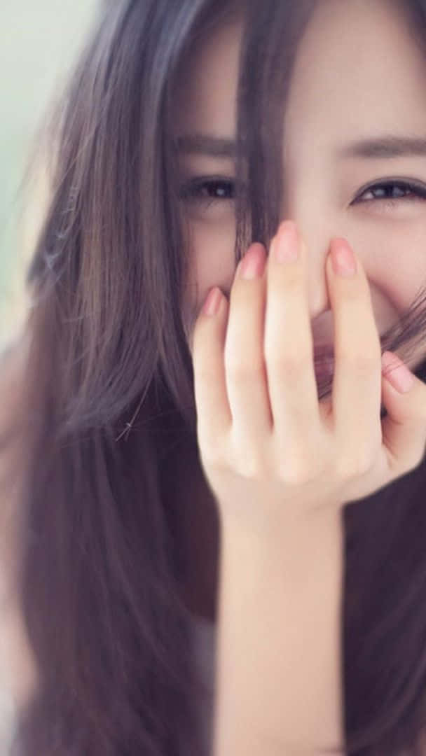 少女風 桌布 壁紙 — 一位長黑髮的年輕女子用手俏皮地遮住嘴巴，露出燦爛的笑容。