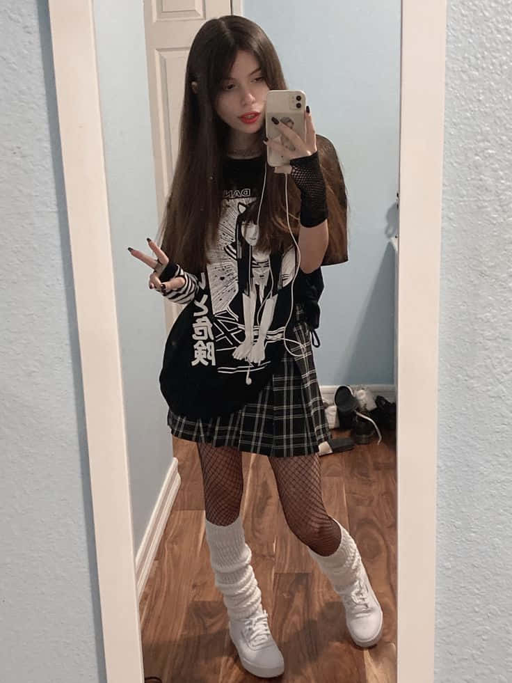 emo 美學 桌布 壁紙 — 一位長黑髮的年輕女性在房間裡穿著圖案T恤、格子裙、魚網襪和白色靴子，對著鏡子自拍。