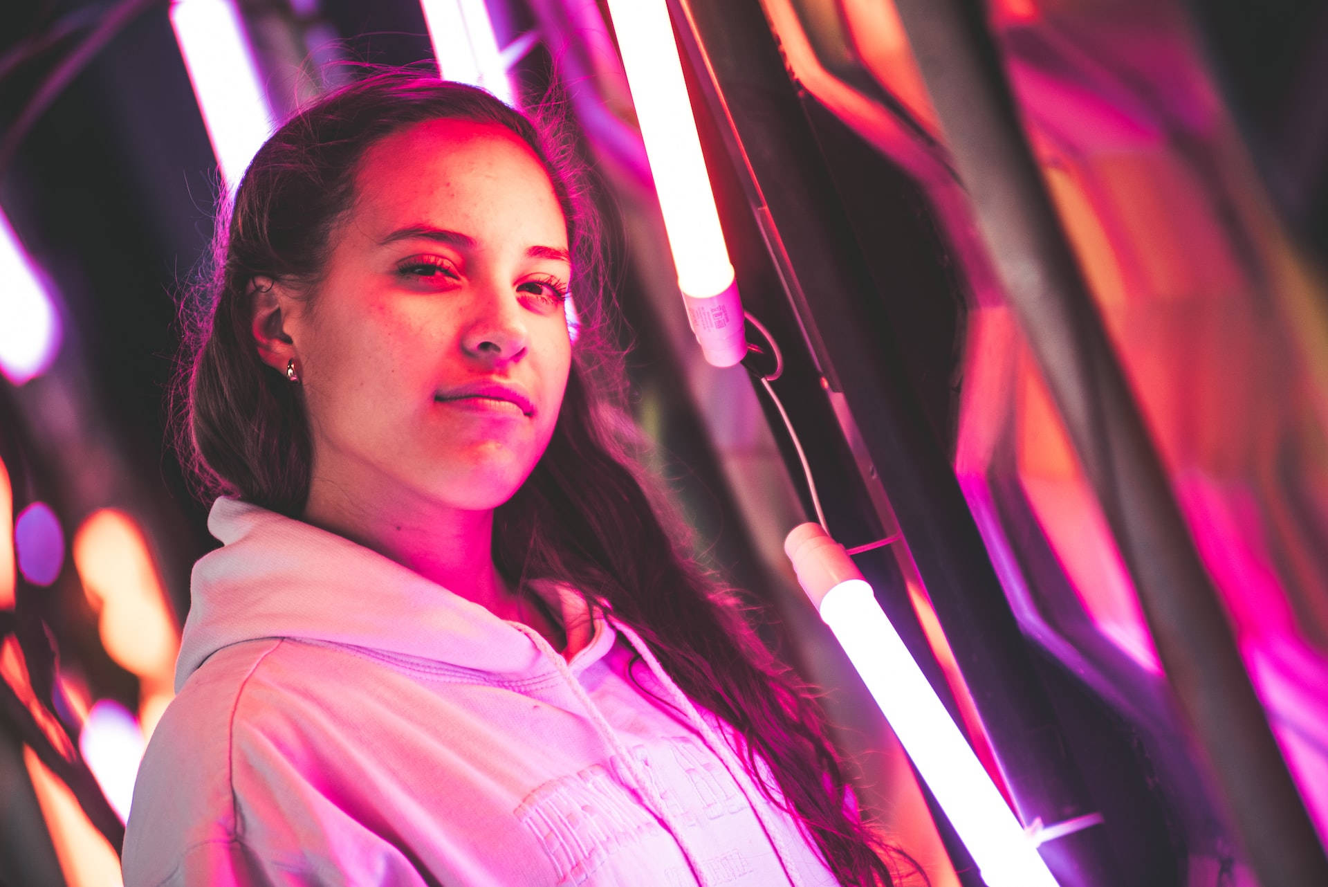 Neon Lights 桌布 壁紙 — 一位長黑髮的年輕女性在未來場景中，平靜地站在鮮豔的粉紅和紫色霓虹燈下。