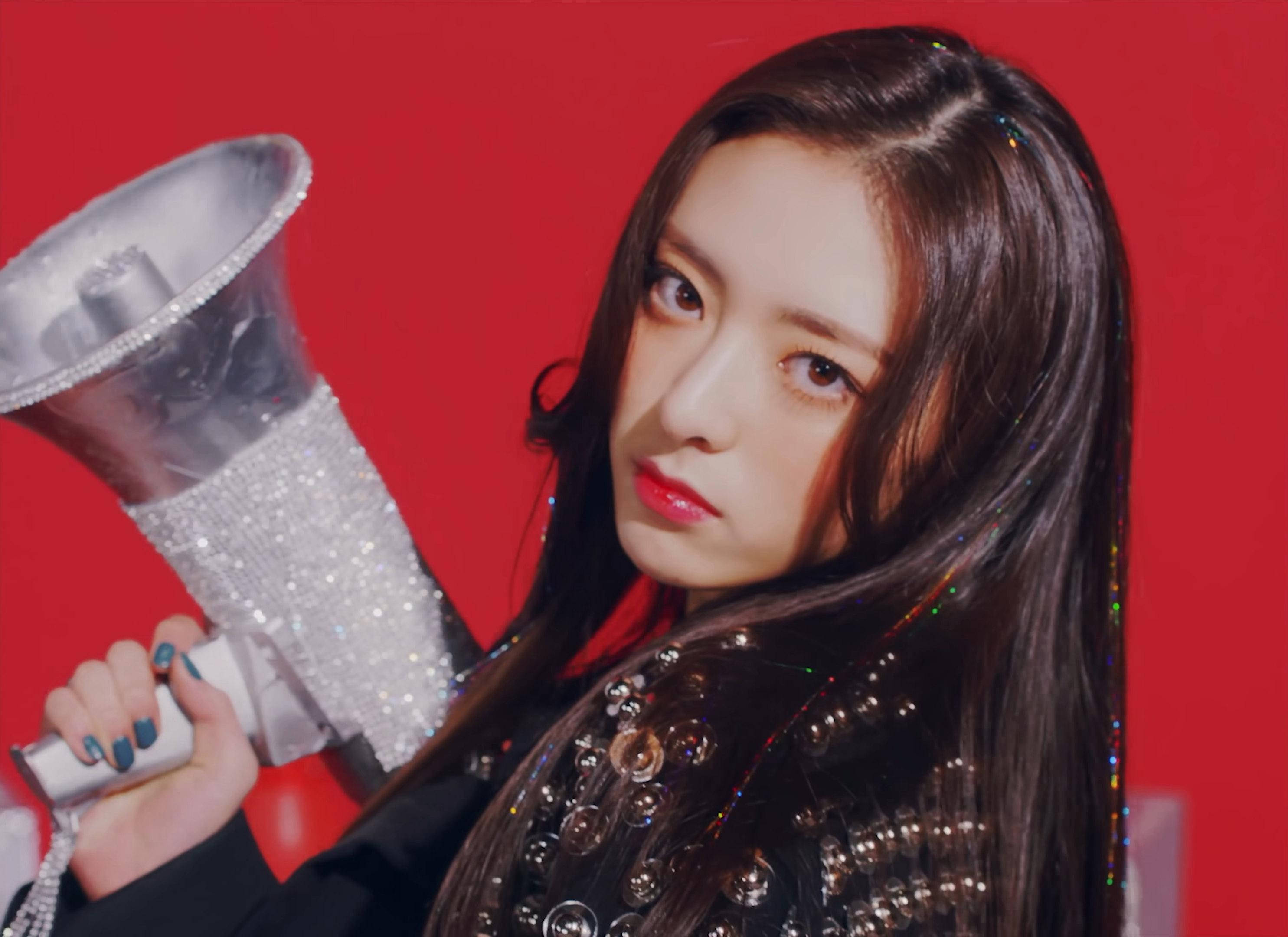 ITZY 桌布 壁紙 — 一位長黑髮的年輕女性在鮮紅色背景前拿著閃閃發光的擴音器。