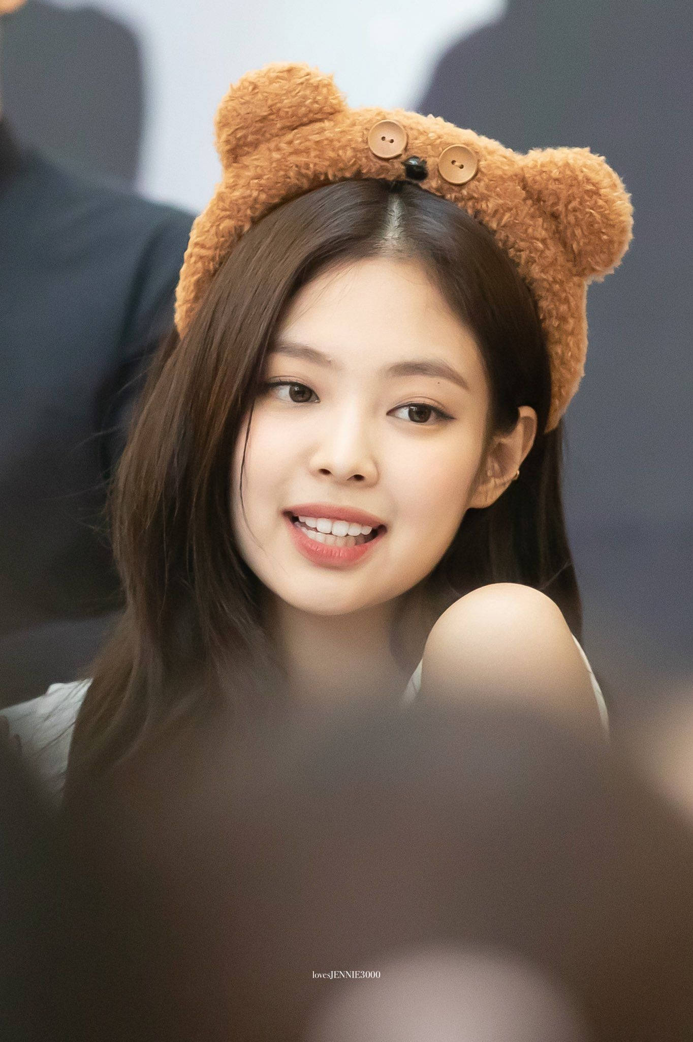 Jennie 桌布 壁紙 — 一位長黑髮的年輕女性戴著毛絨絨的棕色熊耳頭帶，露出溫暖的笑容。