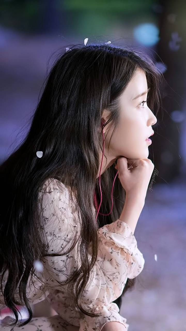 iu phone 桌布 壁紙 — 一位長黑髮的年輕女性戴著紅色耳機聽音樂，在柔和的夜間燈光下若有所思地凝視遠方。