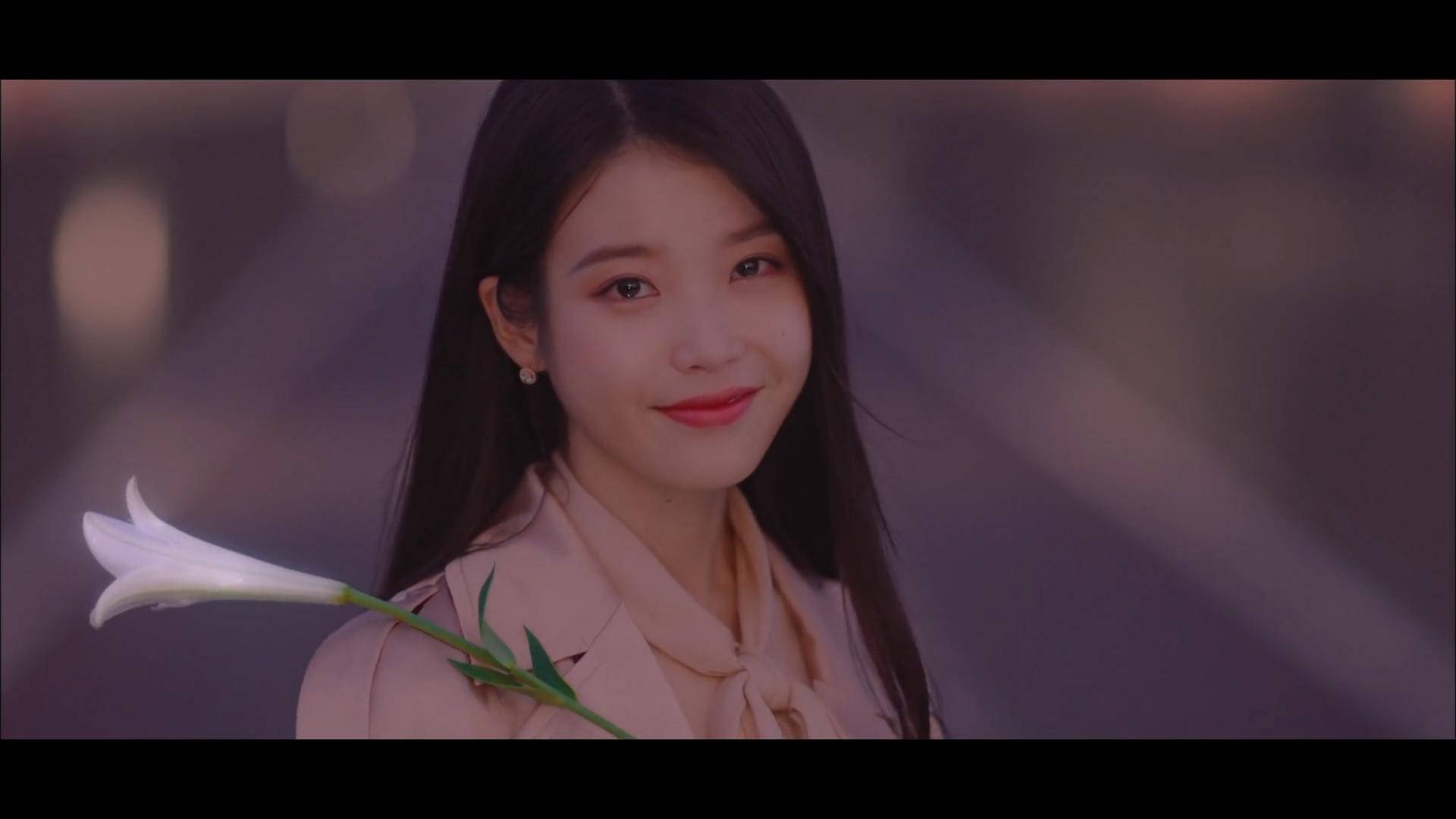 drama 桌布 壁紙 — 一位長黑髮的年輕女性溫柔微笑，手持一朵白色百合花，背景是柔和的紫色散景。
