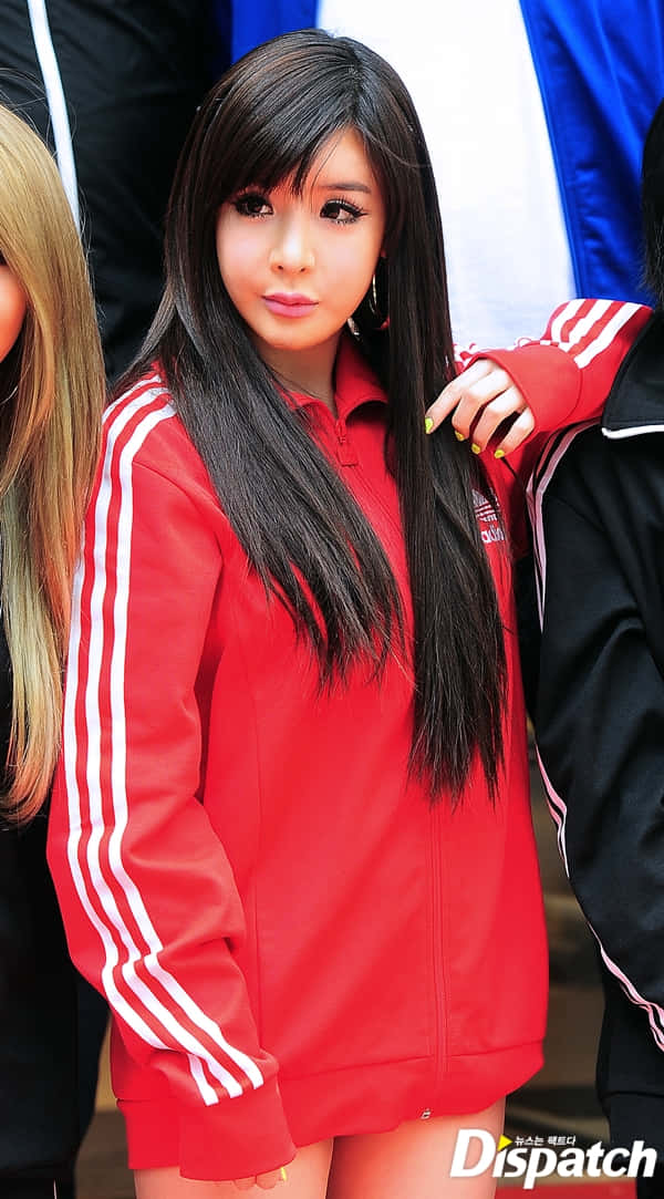 2ne1 桌布 壁紙 — 一位長黑髮的年輕女性穿著帶有白色條紋的亮紅色Adidas運動外套，在戶外擺姿勢。