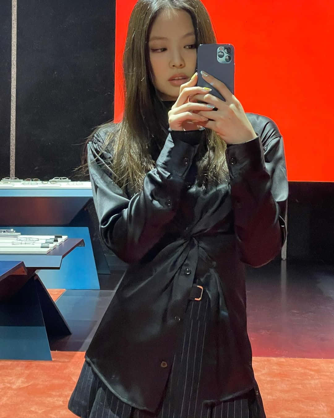 BLACKPINK 桌布 壁紙 — 一位長黑髮的年輕女性穿著時尚的黑色緞面襯衫，在鮮明的紅黑背景下對著鏡子自拍。