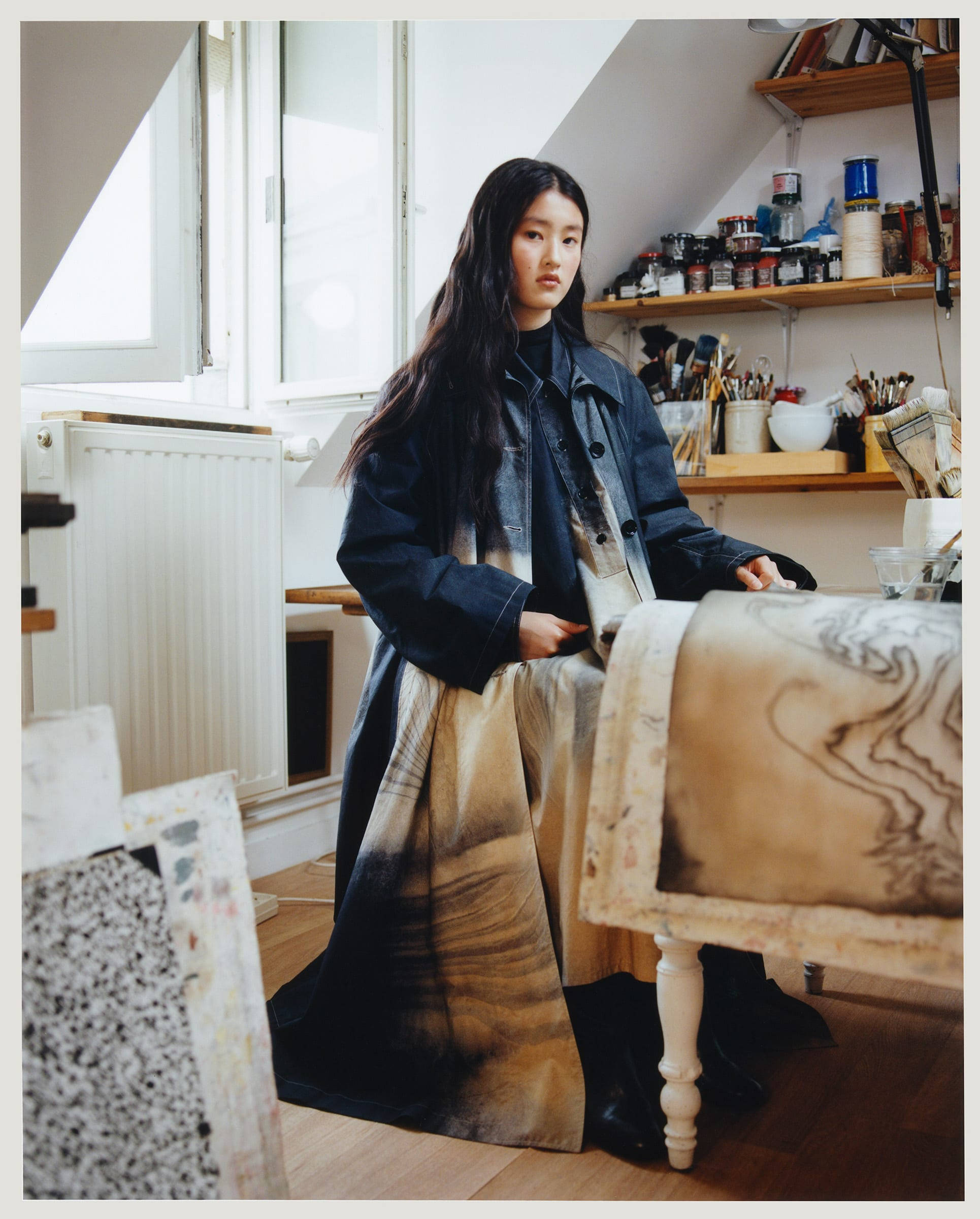 Studio 桌布 壁紙 — 一位長黑髮的年輕女性站在陽光充足的閣樓工作室，周圍環繞著藝術用品和畫作。