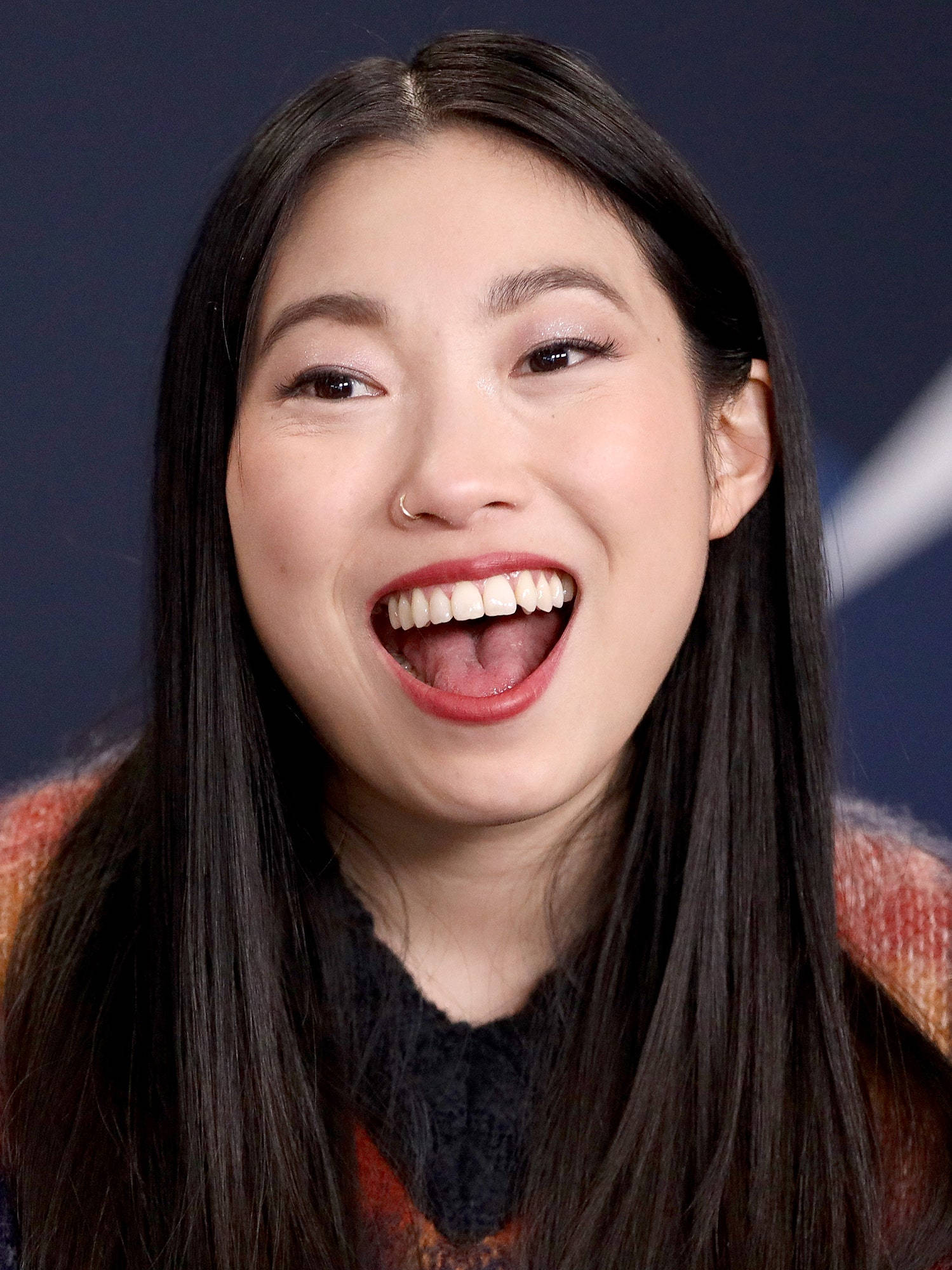 Awkwafina 桌布 壁紙 — 一位長黑髮的快樂女性在深藍色背景下張嘴大笑，露出潔白的牙齒。