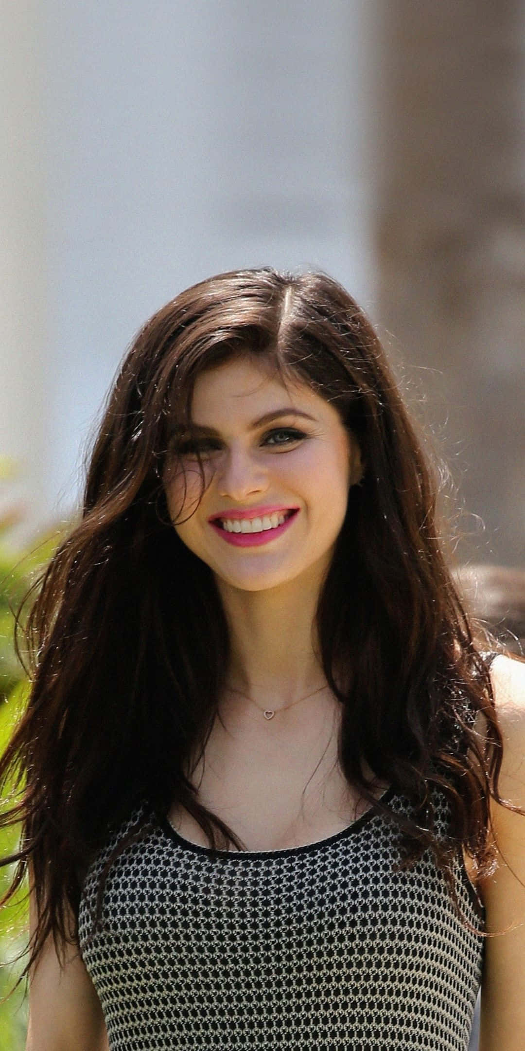 Alexandra Daddario 桌布 壁紙 — 一位長黑髮的燦爛女性在自然光下穿著圖案上衣燦爛微笑。