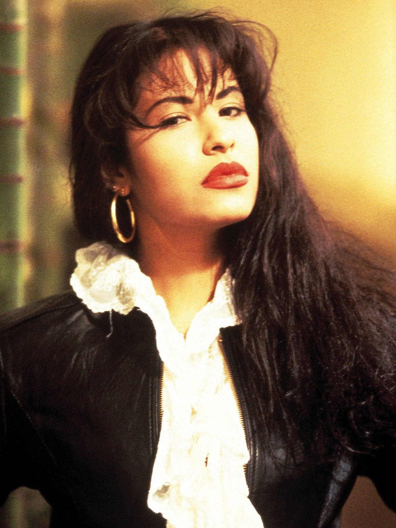 Selena Quintanilla 桌布 壁紙 — 一位長黑髮紅唇的女性，身穿黑色皮夾克內搭白色荷葉邊襯衫，向上凝視。