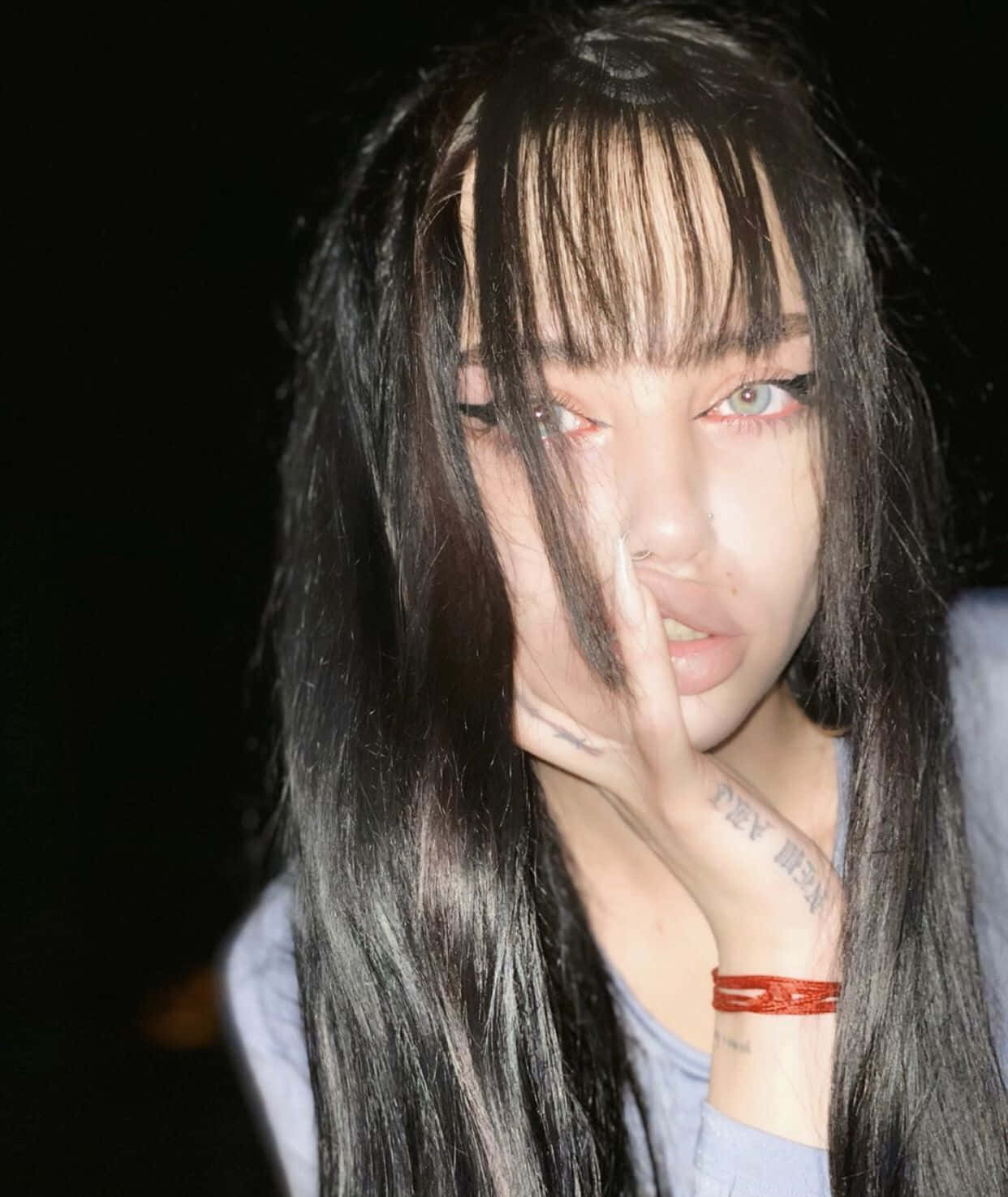 垃圾美學 桌布 壁紙 — 一位長黑髮紅眼女性的特寫肖像，她的手部分遮擋著臉，背景為黑色。