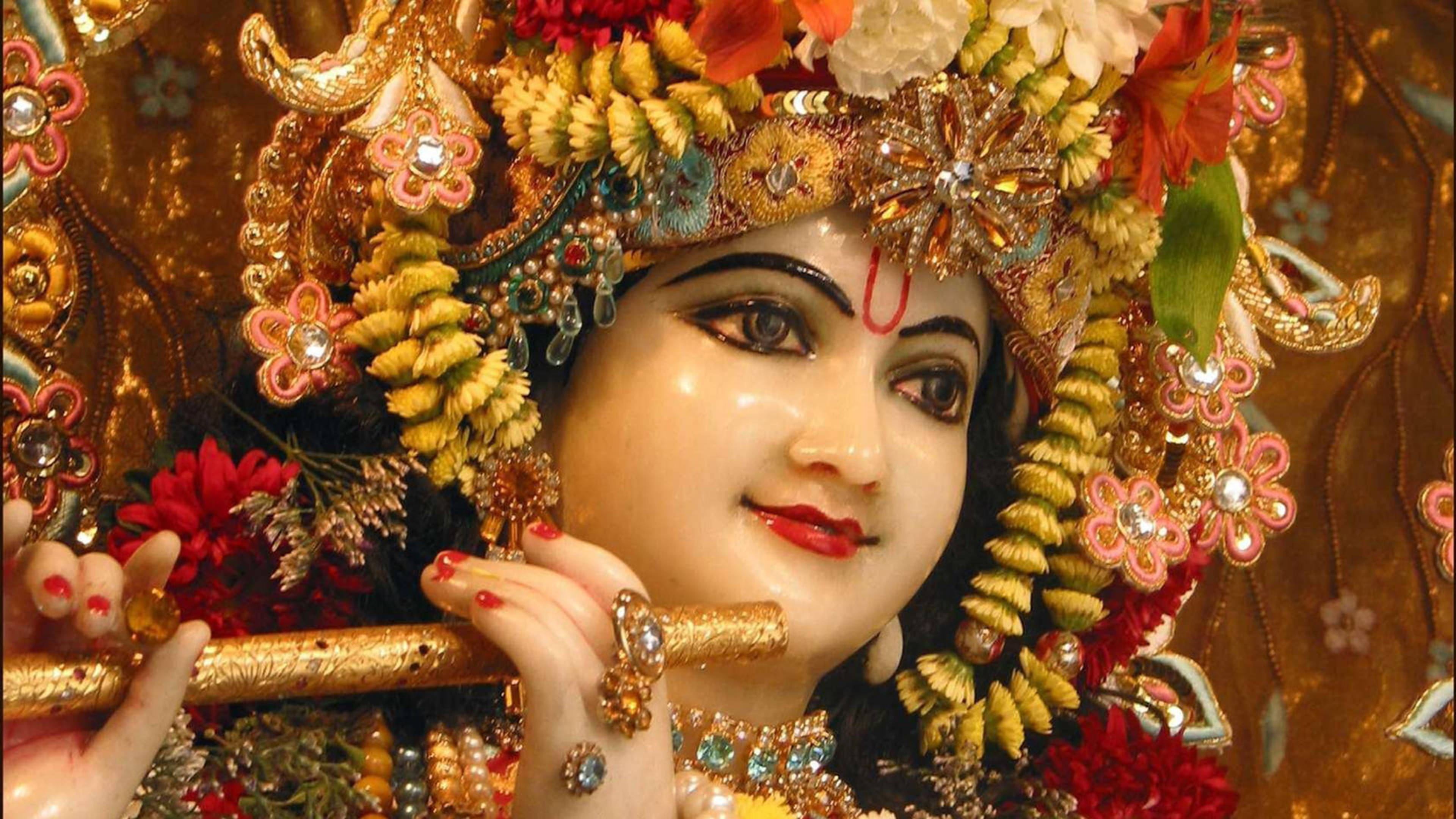 krishna ji 桌布 壁紙 — 一位閃耀的神祇，飾有金色珠寶和色彩繽紛的花環，手持長笛，指甲塗有顏色。