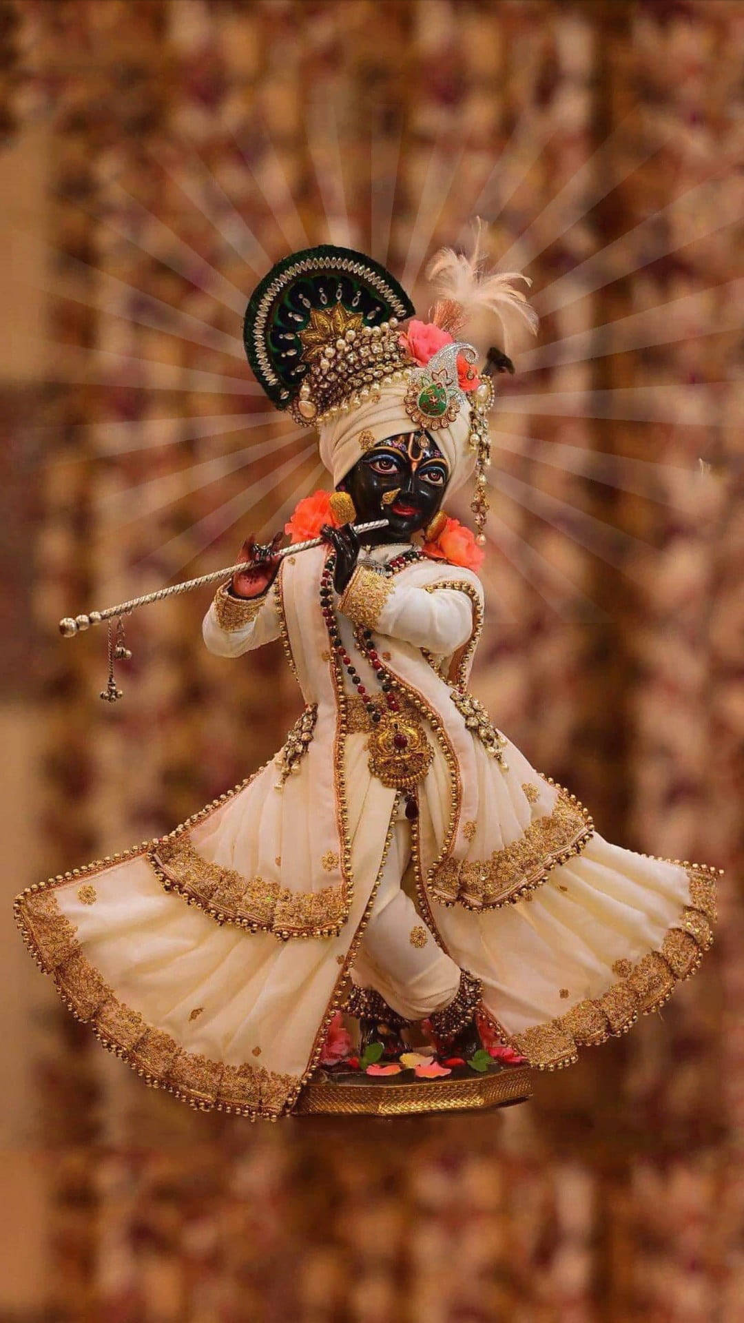 krishna iPhone 桌布 壁紙 — 一位閃耀的黑皮膚神祇，身穿華麗的奶油色和金色服飾，吹奏長笛，背後散發出神聖的光芒。