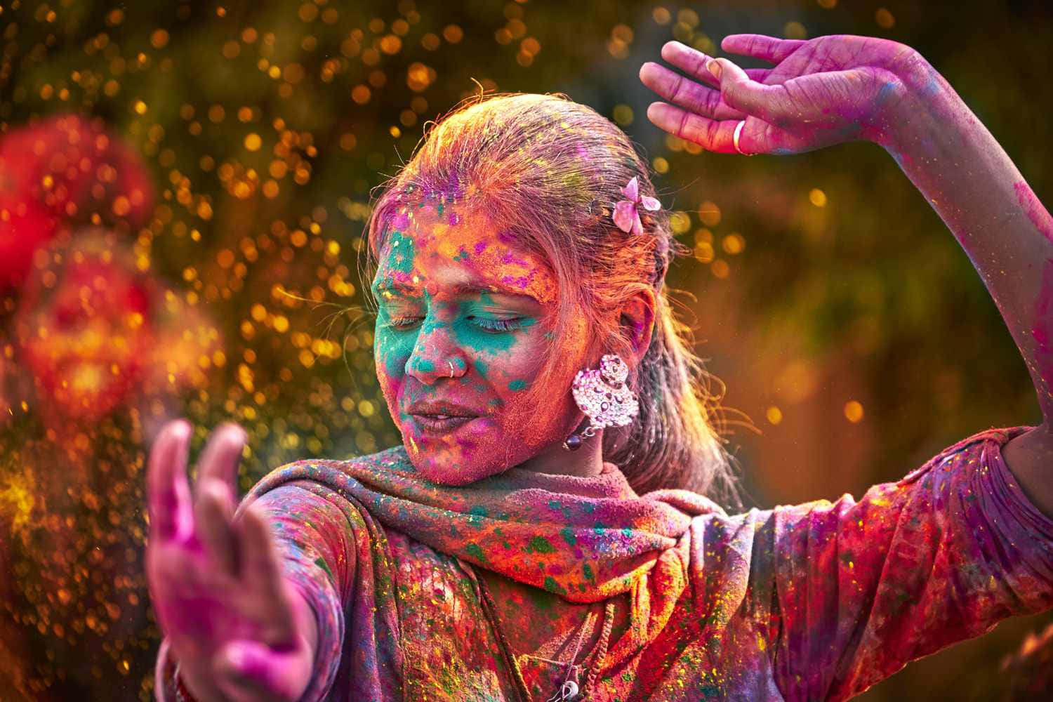 Holi 桌布 壁紙 — 一位閉著眼睛、雙臂伸展的女性，在節日慶祝活動中快樂地被鮮豔的彩色粉末覆蓋。