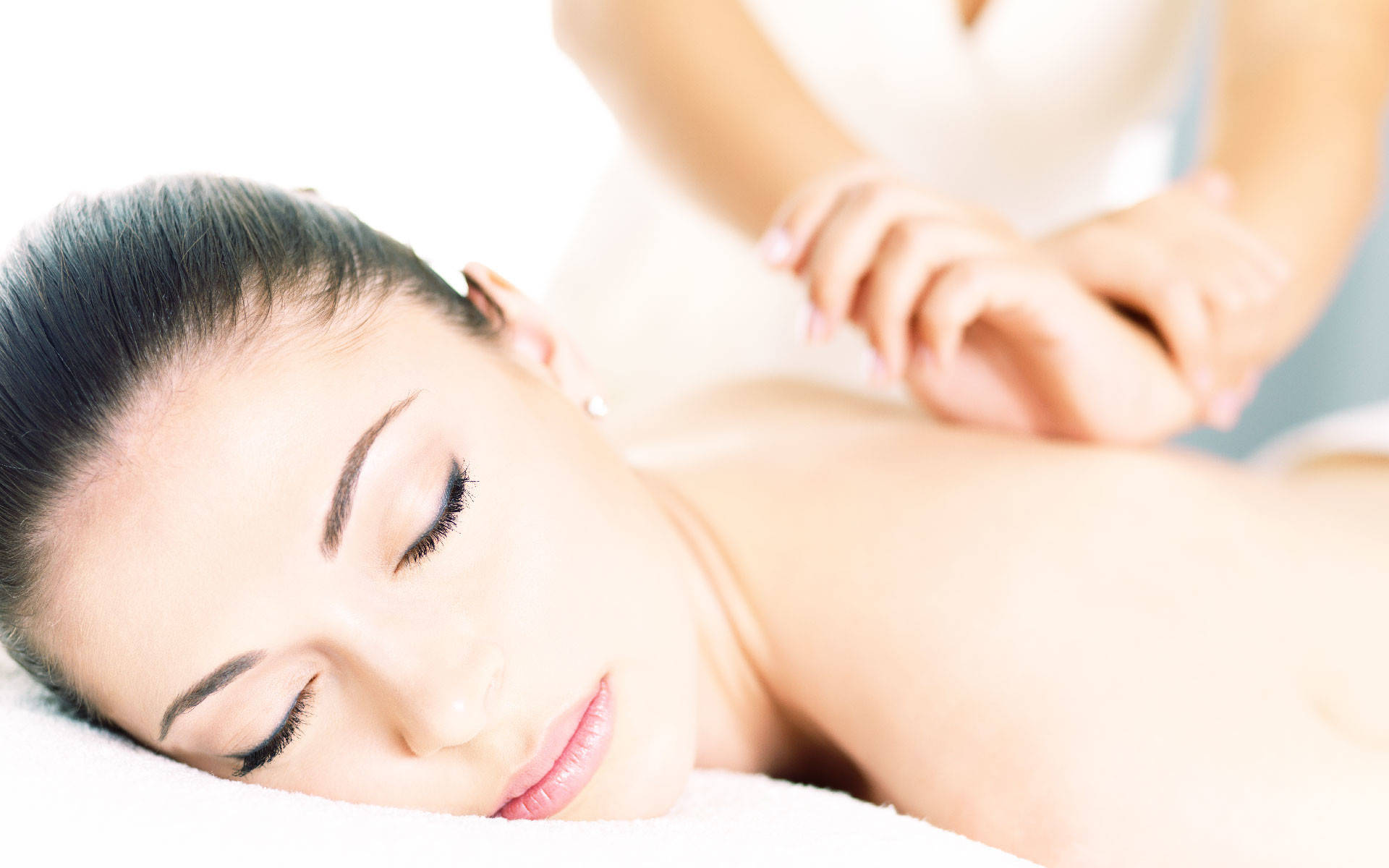 Salon 桌布 壁紙 — 一位閉著眼睛的寧靜女性在明亮的白色水療環境中享受舒緩的背部按摩。