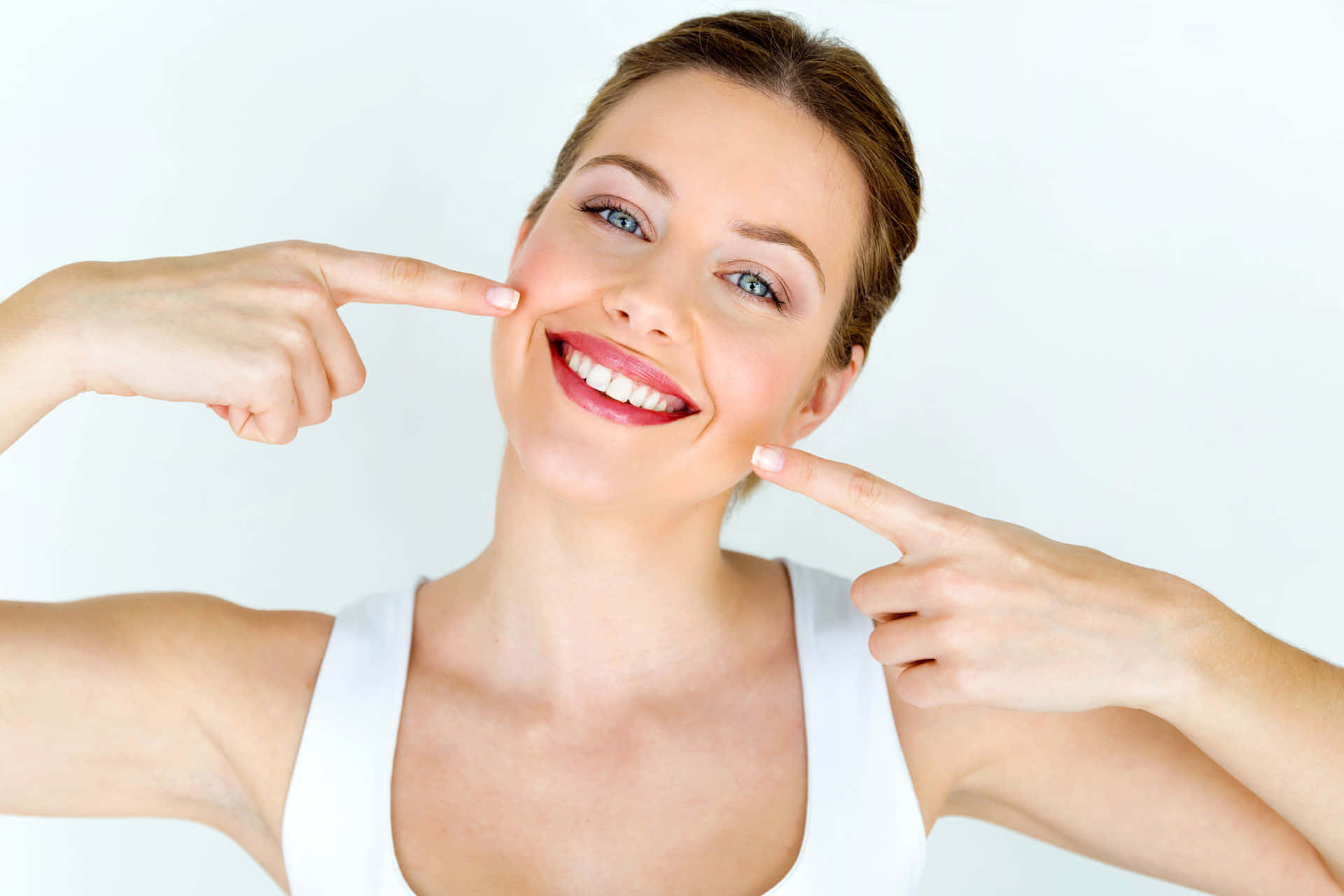 Fake Smile 桌布 壁紙 — 一位開心的女士穿著白色上衣，在純白背景前燦爛微笑，同時指向她完美的牙齒。