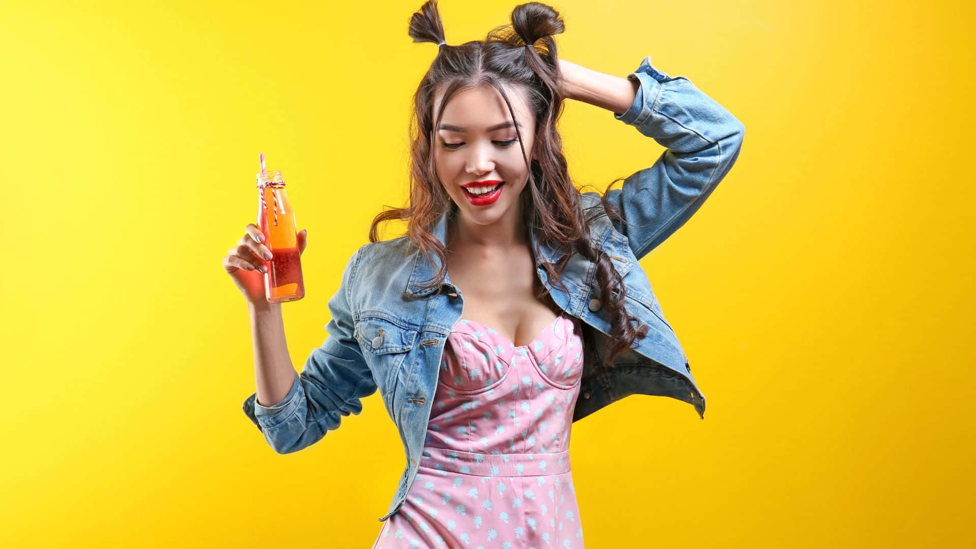 Hipster 桌布 壁紙 — 一位開心的年輕女性紮著雙丸子頭，在明亮的黃色背景前微笑著手持一瓶柳橙汁玻璃瓶。